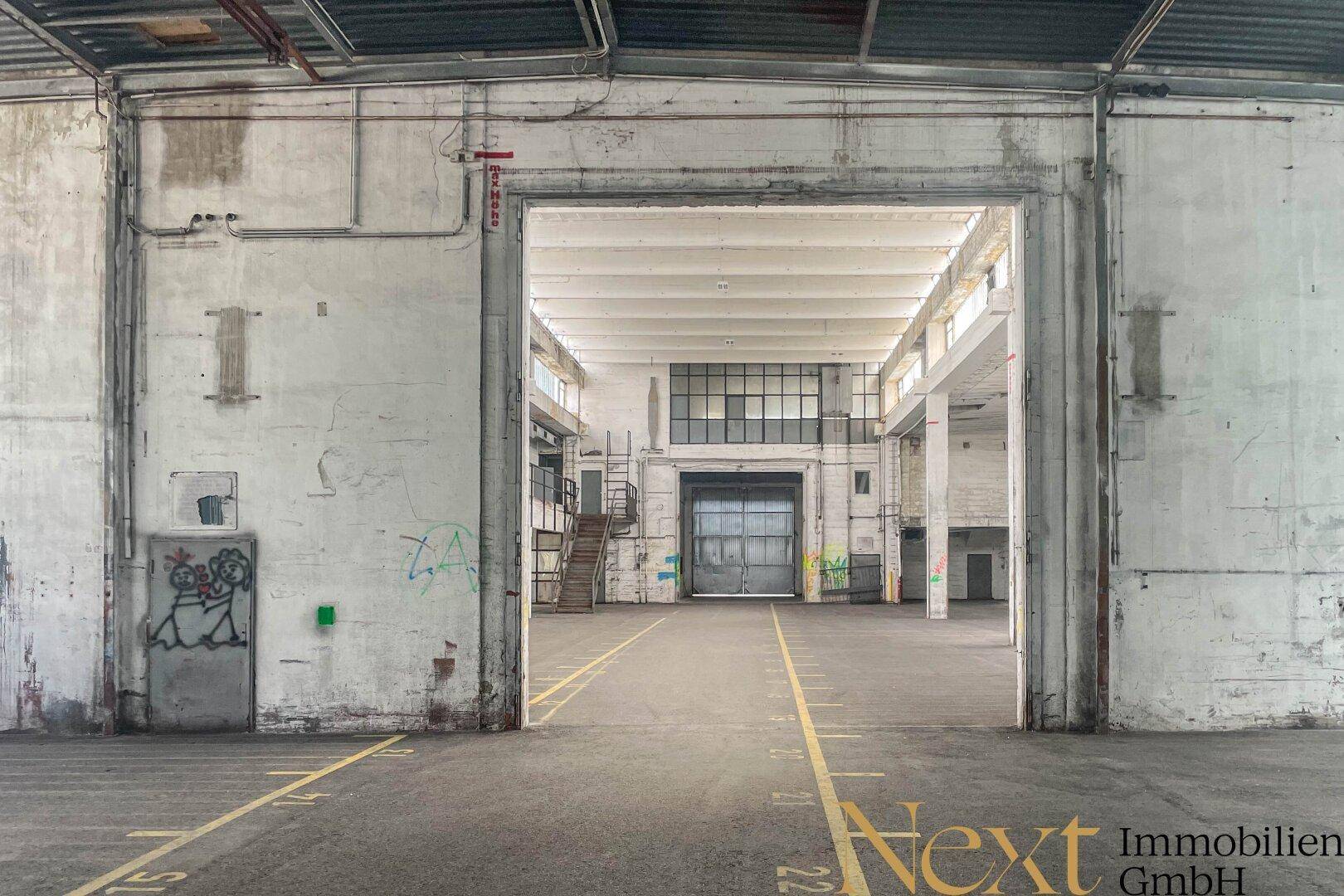 Eingangsbereich einer großen Industriehalle mit Rolltor, hohen Decken und sichtbaren Markierungen am Boden.