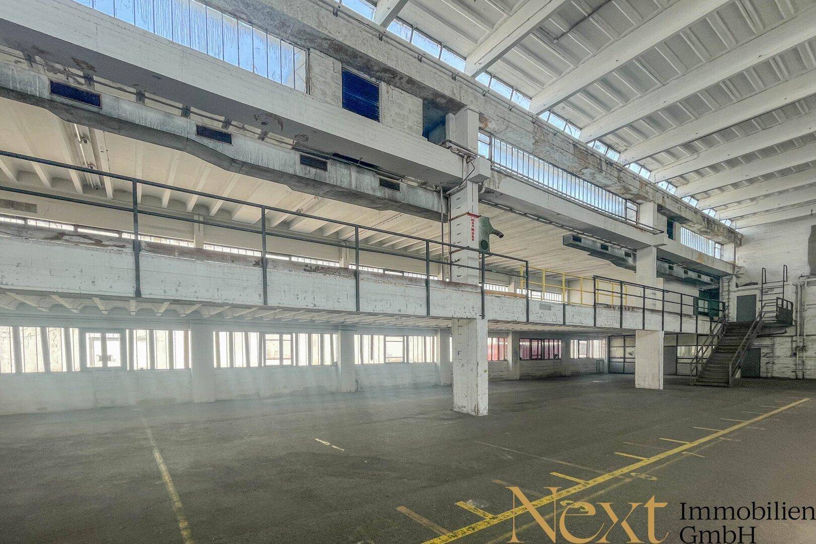 Helle Industriehalle mit hohen Decken, großen Fensterfronten und einer umlaufenden Galerie.