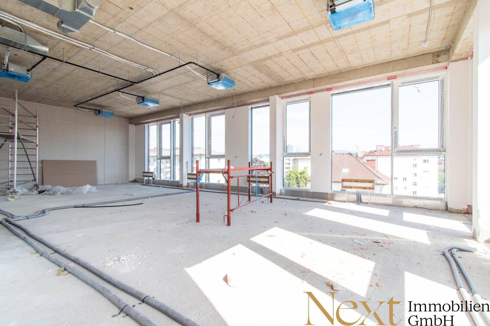 Heller Gewerberaum im Rohbau mit unverputzten Wänden, Betonboden und Blick auf die Stadt.