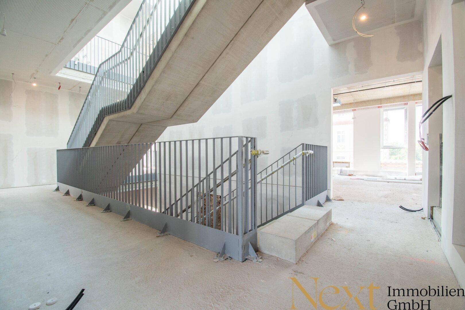Moderne Betontreppe mit elegantem Metallgeländer in einem im Bau befindlichen Gebäude mit hohen Decken.