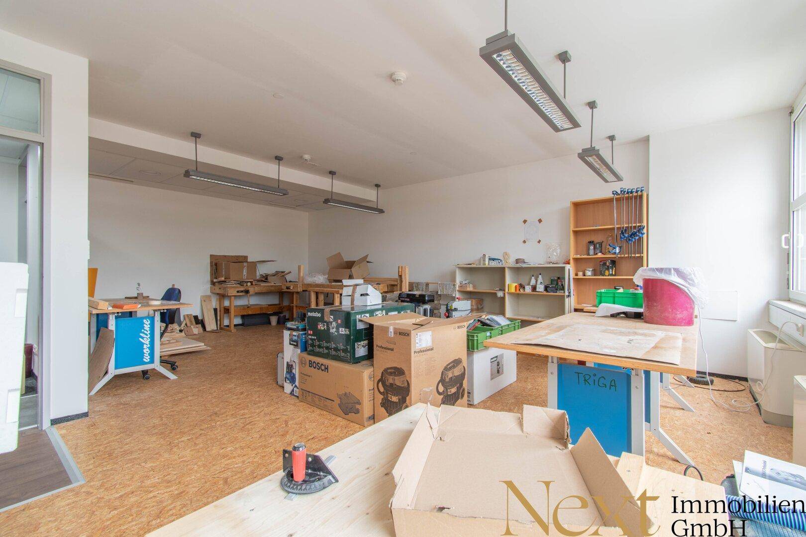Werkstattraum mit Holzböden, Arbeitstischen und Regalen, ideal für handwerkliche Tätigkeiten oder Lagerung.