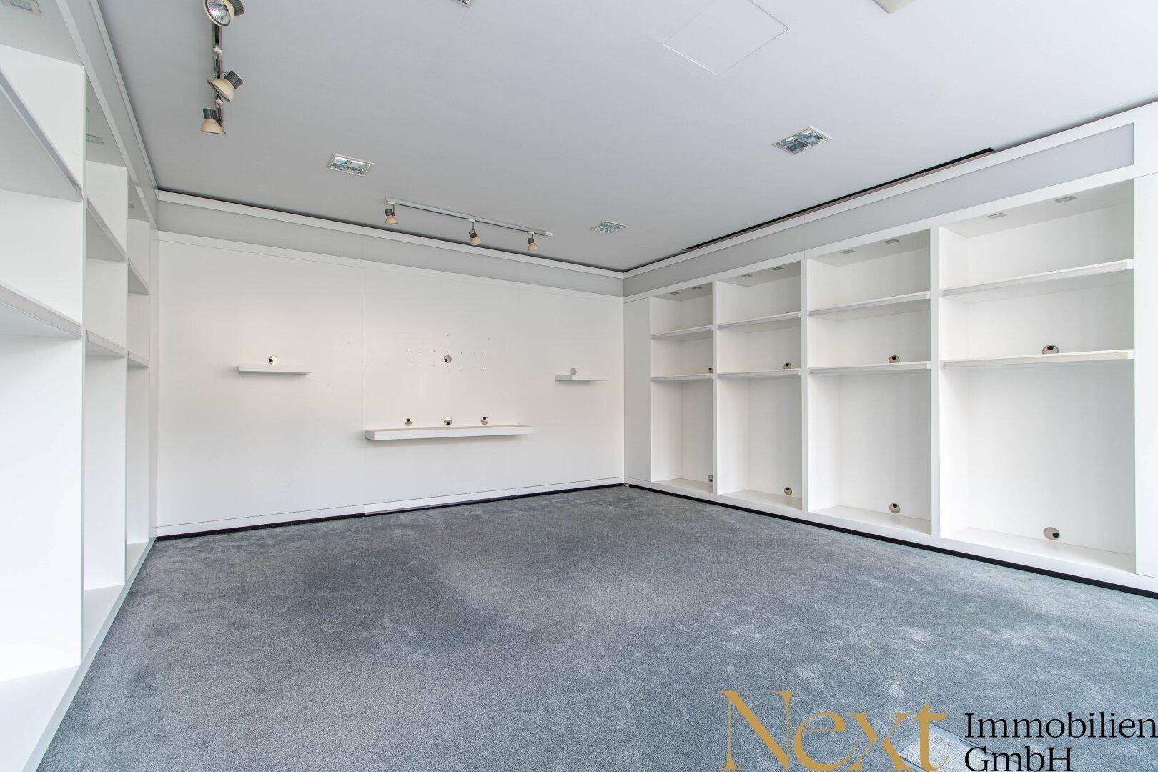 Gewerberaum mit integrierten weißen Regalen und grauem Teppichboden, ideal für Laden oder Büro.