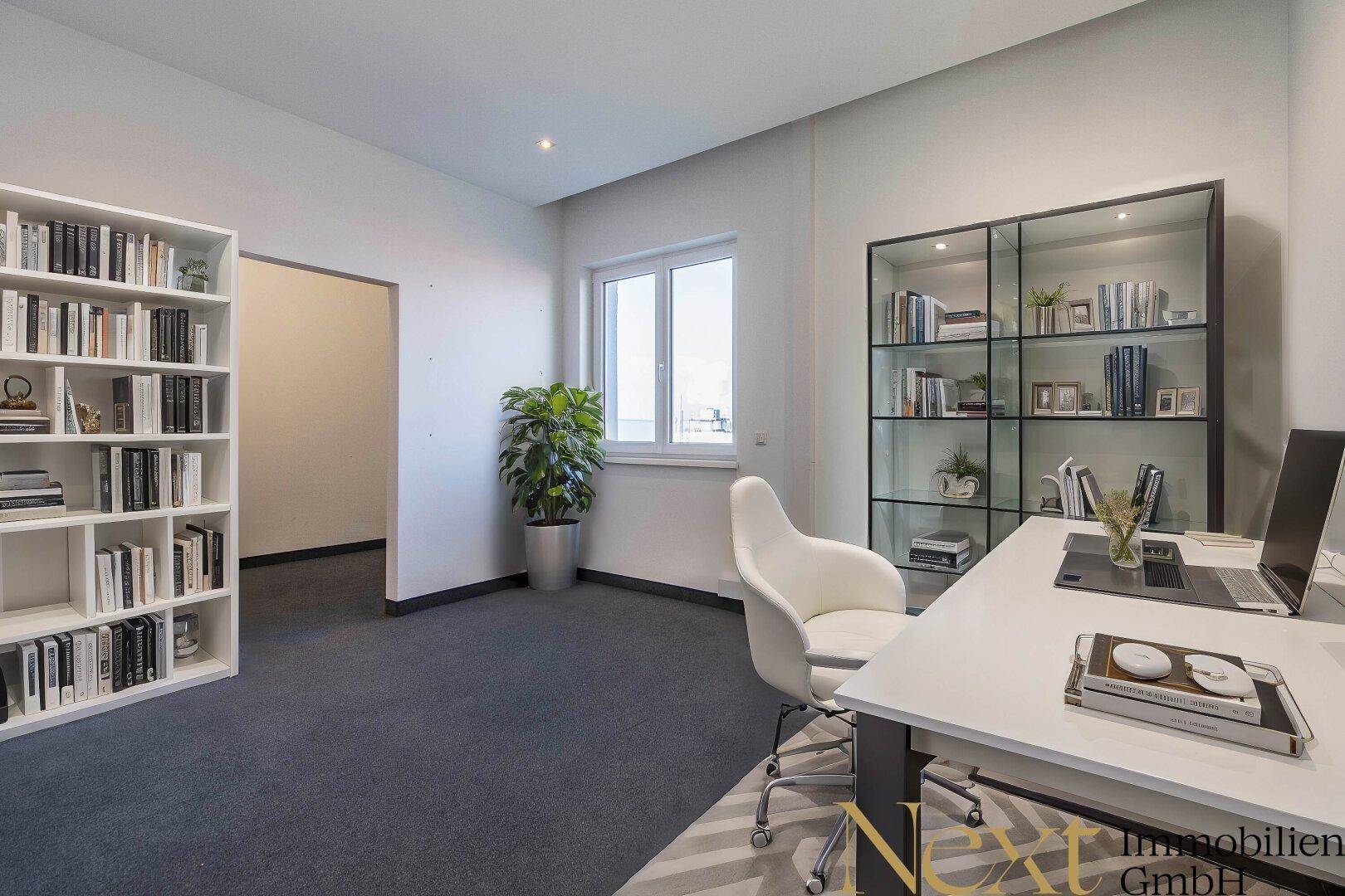 Helles Büro mit Teppichboden, Bücherregalen und einem Fenster, das viel Tageslicht hereinlässt.