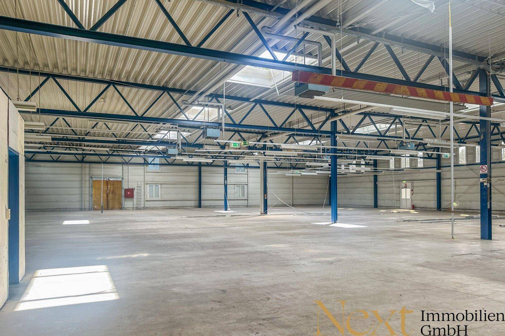 Geräumige, leere Lagerhalle mit hoher Decke, sichtbaren Stahlträgern und Betonboden.