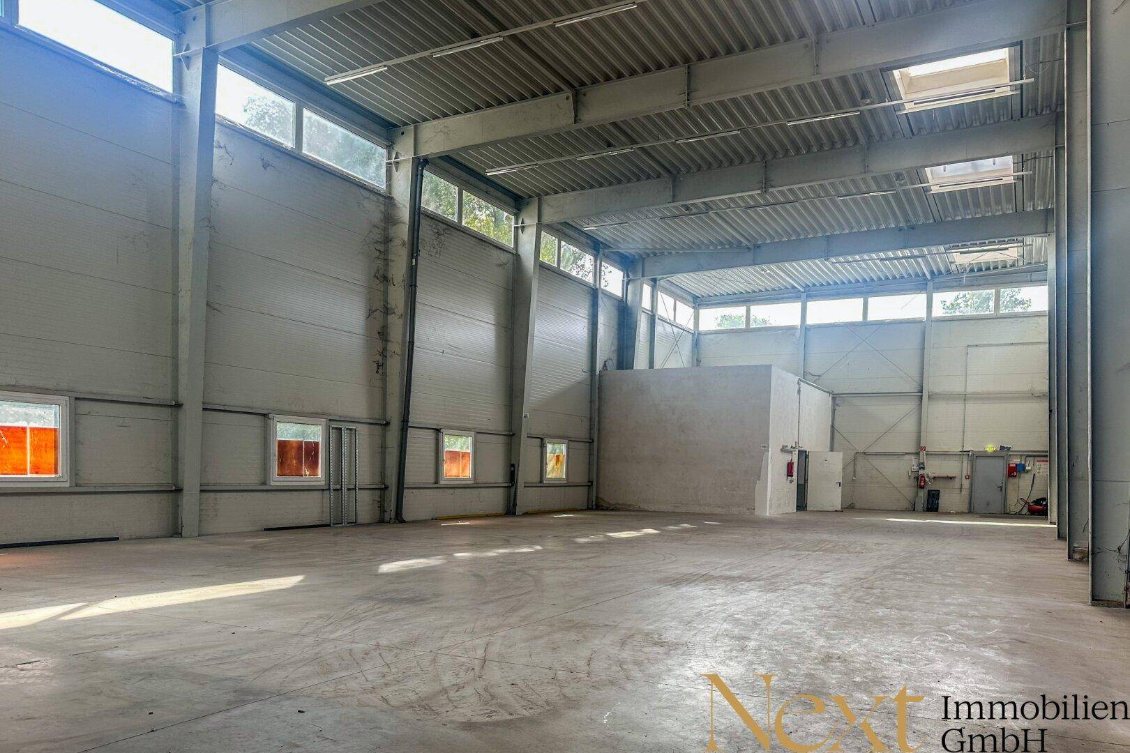 Helle Lagerhalle mit hohen Wänden, großen Fenstern und einem strapazierfähigen Betonboden.