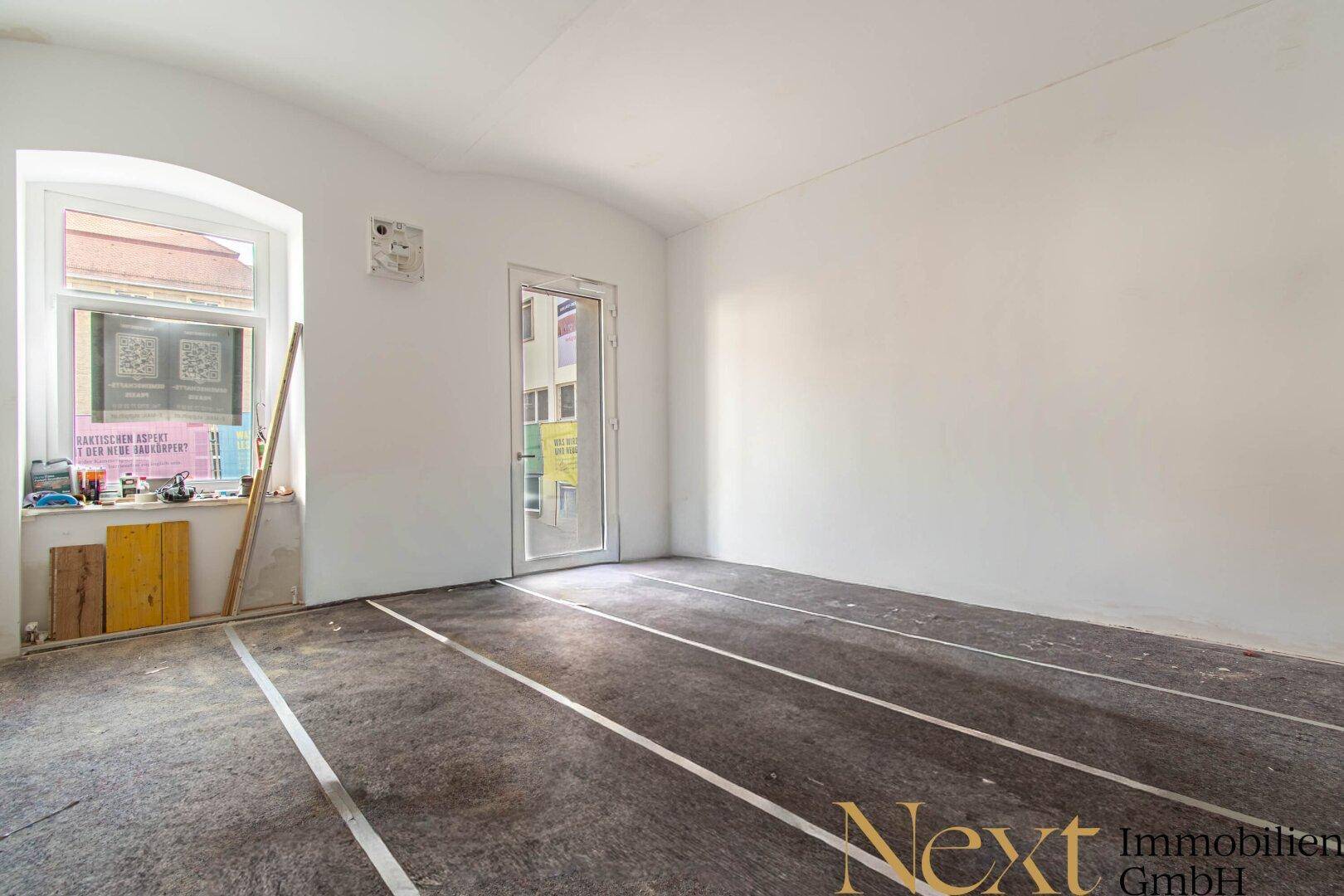 Leerer Raum in Renovierung mit provisorischem Bodenbelag und Fenster, bereit für den Ausbau.