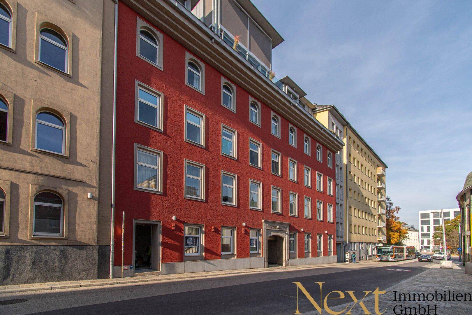 Historisches Gebäude mit markanter roter Fassade und vielen Fenstern an einer städtischen Straße.