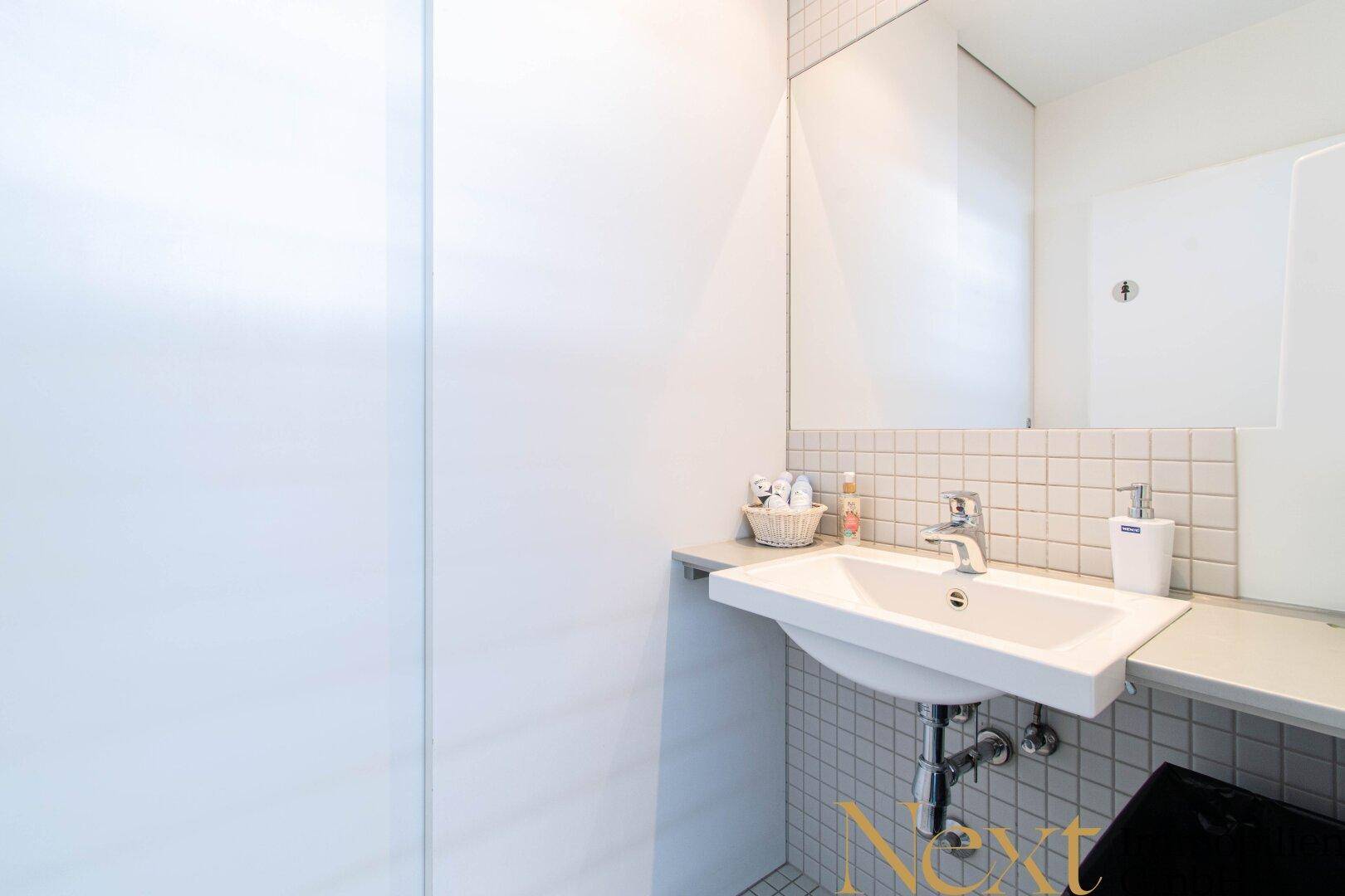 Sauberer Sanitärbereich mit einem Waschbecken, Spiegel und weißen Fliesen, ideal für den täglichen Gebrauch im Büro.