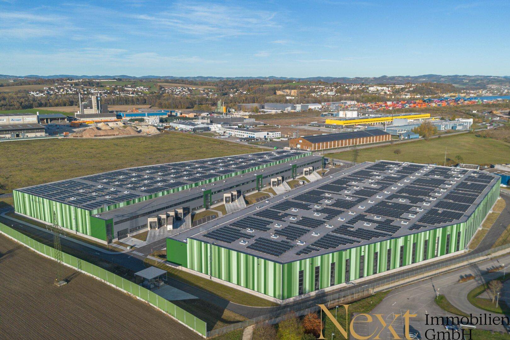 Luftaufnahme von zwei großen Industriehallen mit Photovoltaikanlagen auf den Dächern, eingebettet in eine Industrielandschaft.