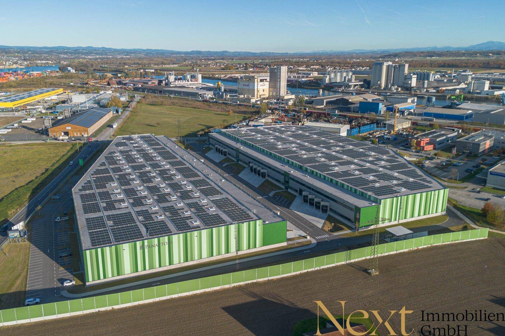 Panoramablick aus der Luft auf zwei große Gewerbegebäude mit Solaranlagen und die umliegende Industrielandschaft.