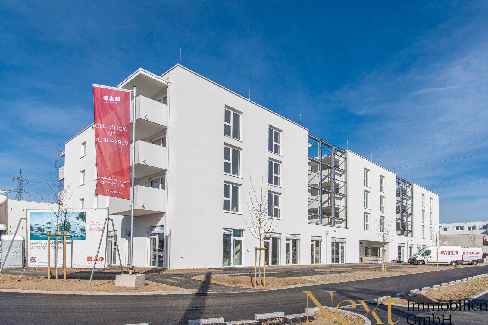Neues, helles Wohn- und Geschäftsgebäude mit moderner Architektur und Außenparkplätzen.
