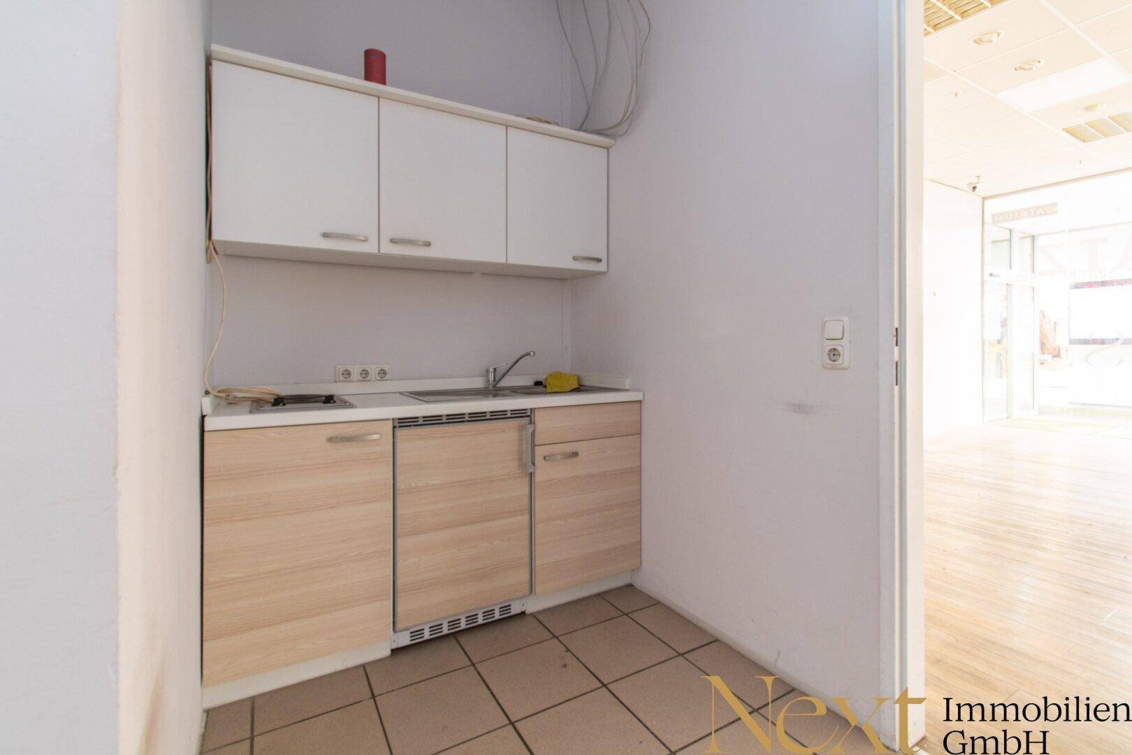 Funktionale Küchenzeile mit weißen Oberschränken, hellem Holzdekor und Fliesenboden, ideal für eine kleine Pause.