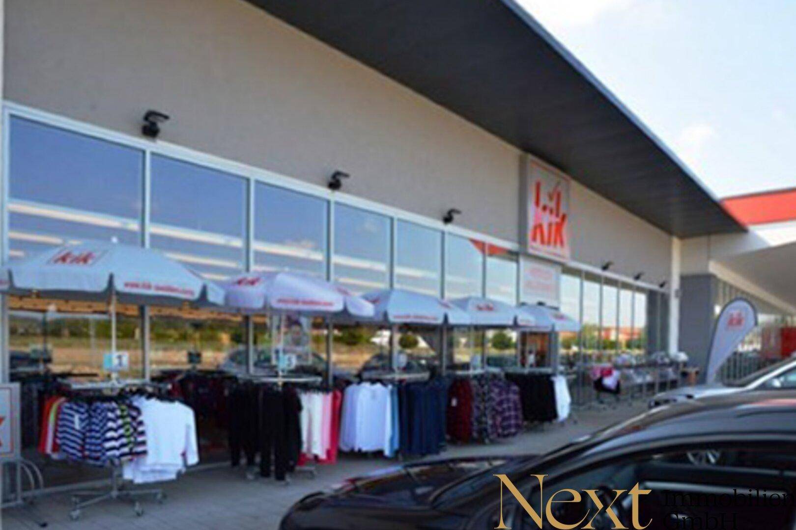 Moderne Ladenfront mit großen Schaufenstern und Outdoor-Warenpräsentation unter Sonnenschirmen.