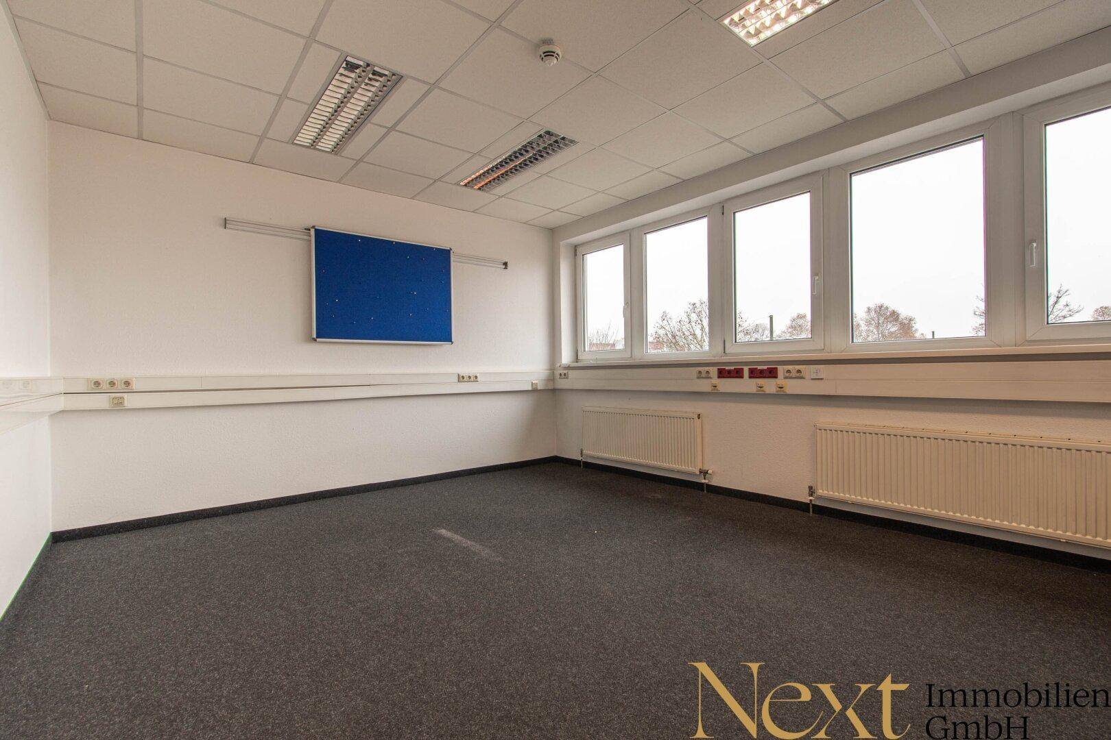 Helles Büro mit großen Fenstern, grauen Teppichboden und funktionaler Ausstattung, ideal für Arbeitsbereiche.