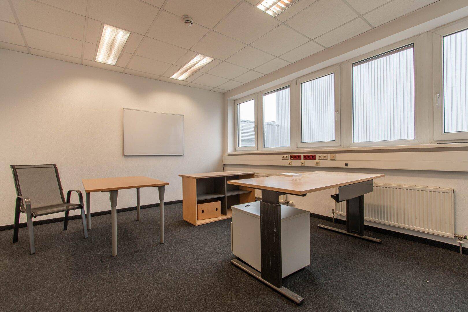 Geräumiges Büro mit großen Fenstern, Teppichboden und funktionalen Büromöbeln für eine angenehme Arbeitsatmosphäre.