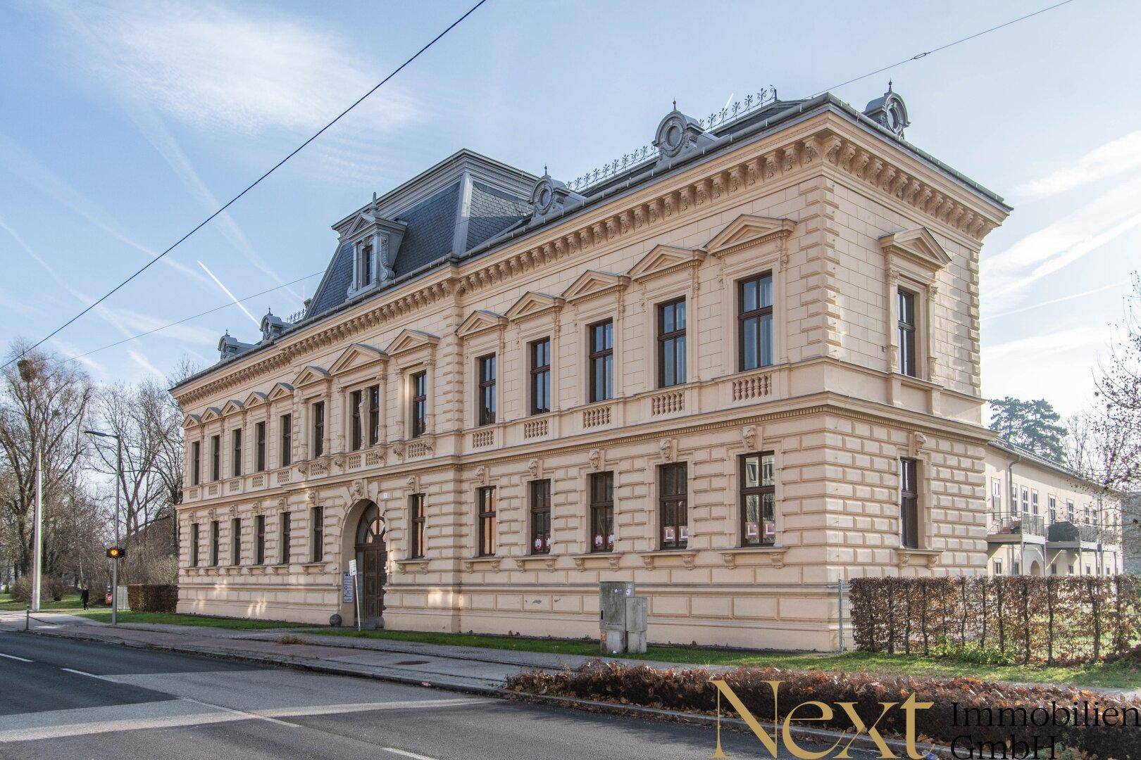 Historisches Gebäude mit klassischer Architektur, vielen Fenstern und einer gepflegten Fassade an einer Straße.