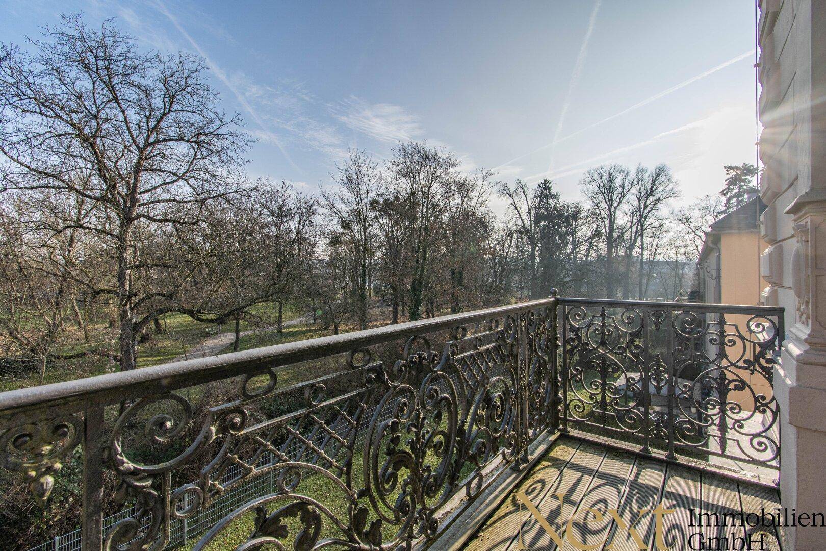 Historischer Balkon mit schmiedeeisernem Geländer und Blick auf einen grünen Park.