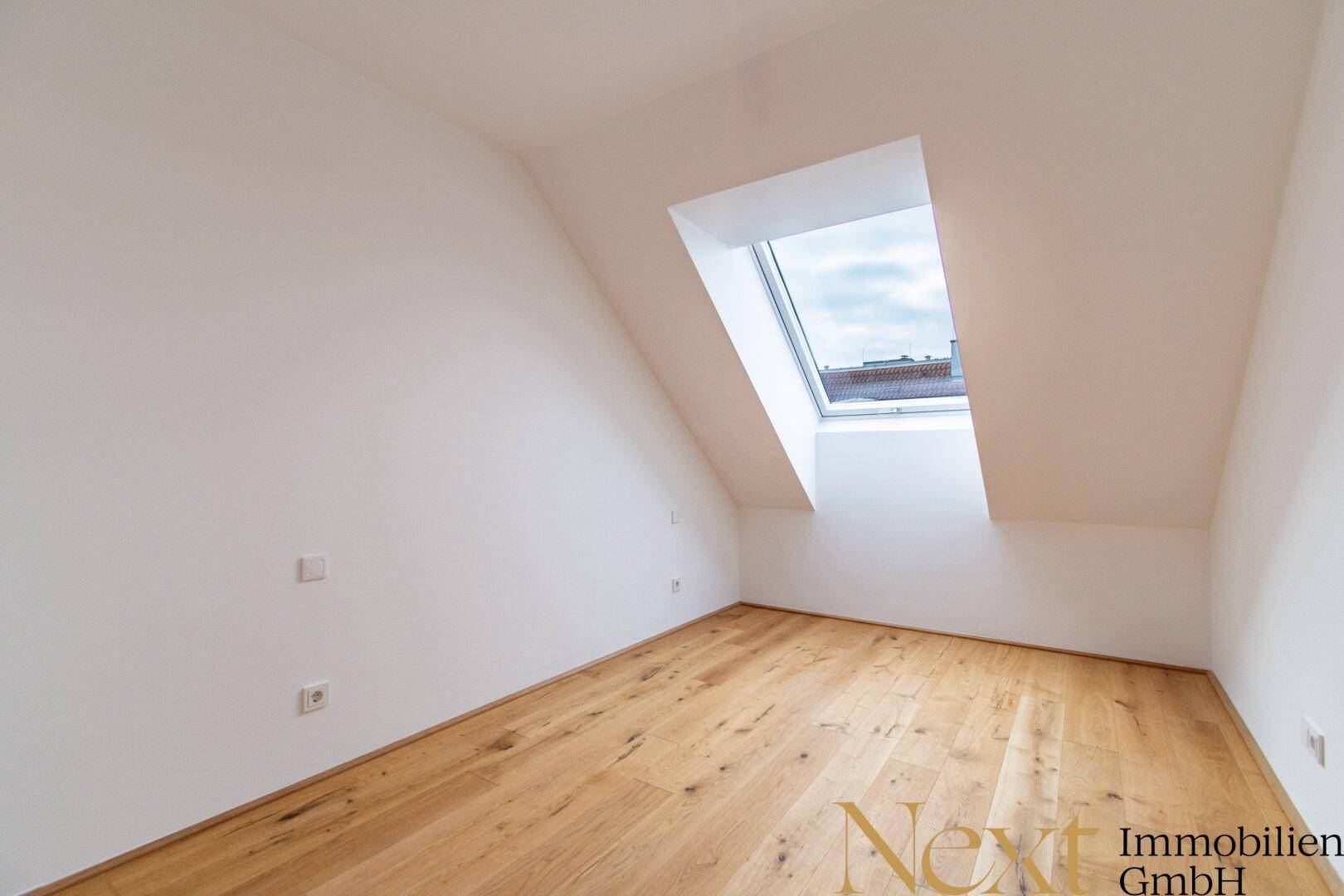 Leeres Schlafzimmer im Dachgeschoss mit Holzboden und großem Dachfenster.