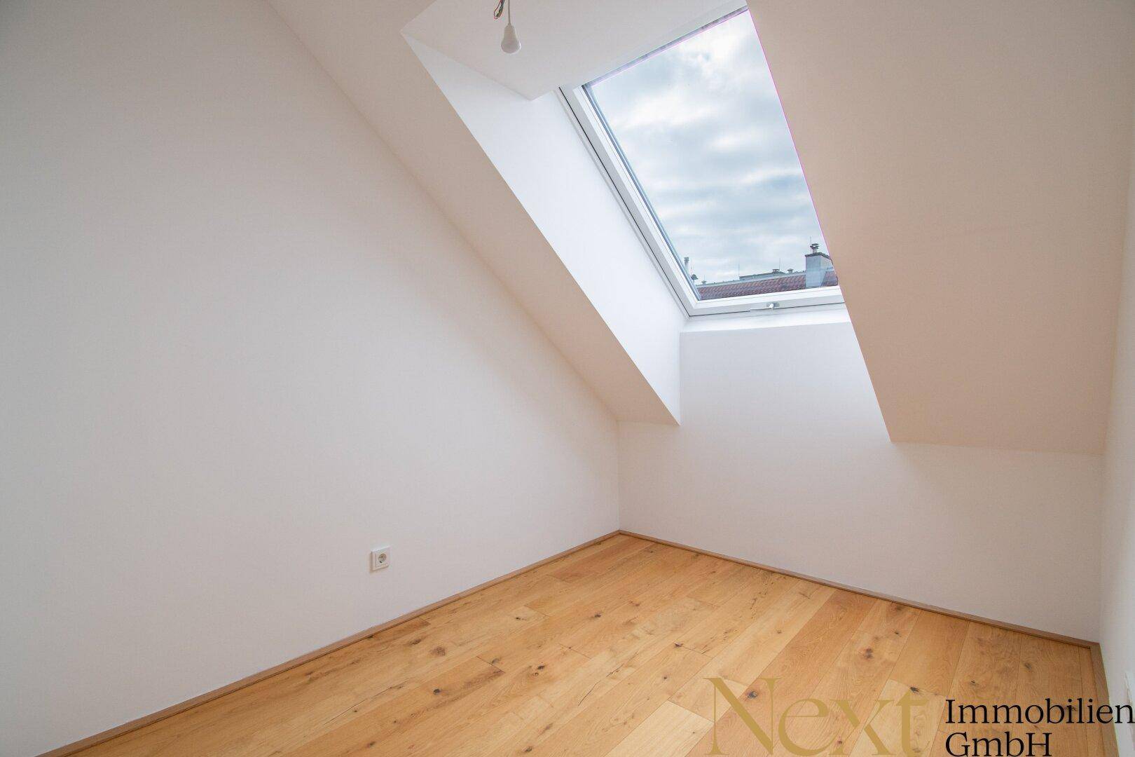 Helles Dachgeschosszimmer mit Holzboden und schrägem Dachfenster, ideal als Schlafzimmer.