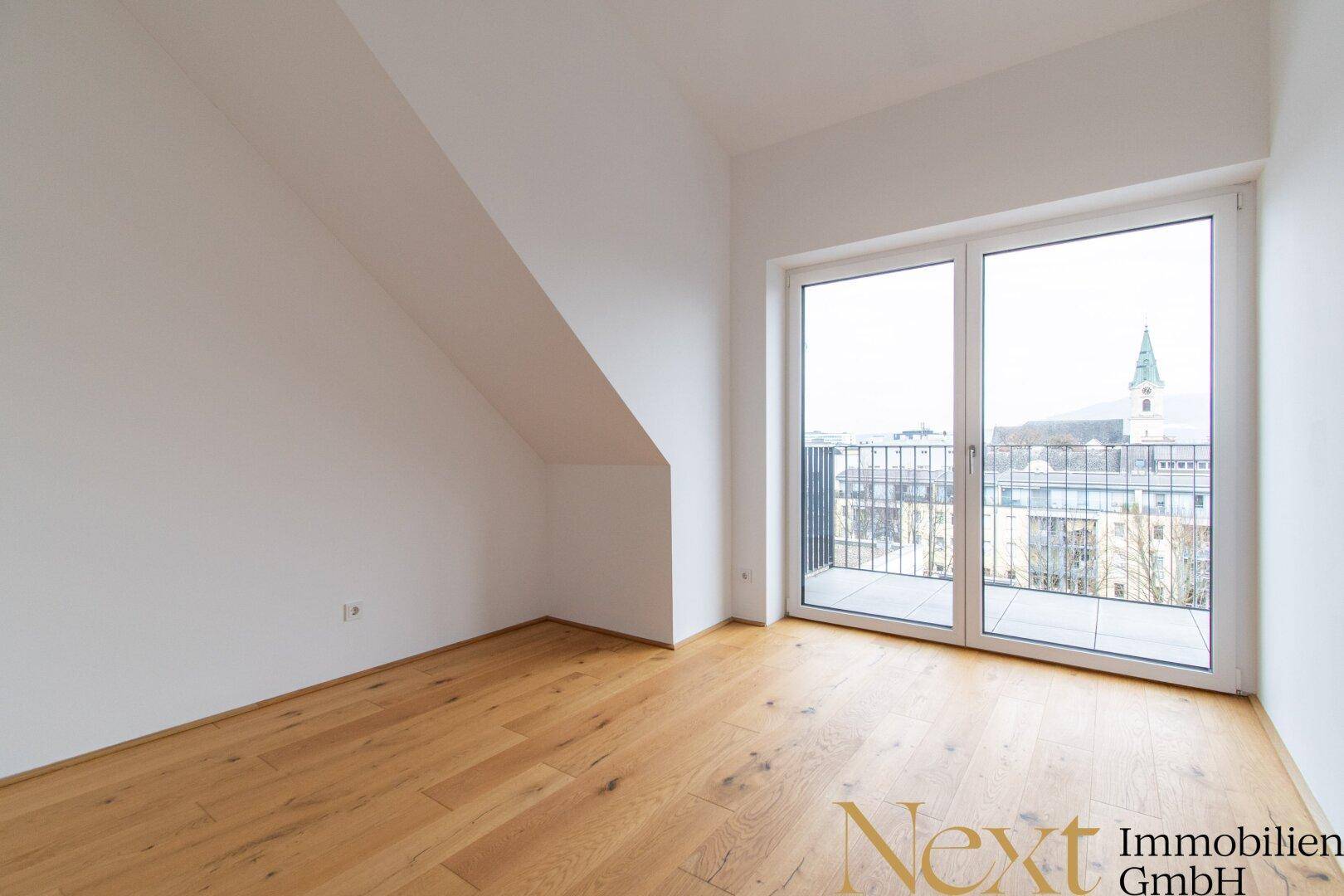 Helles Schlafzimmer mit Holzboden, Dachschräge und Zugang zu einer Terrasse.