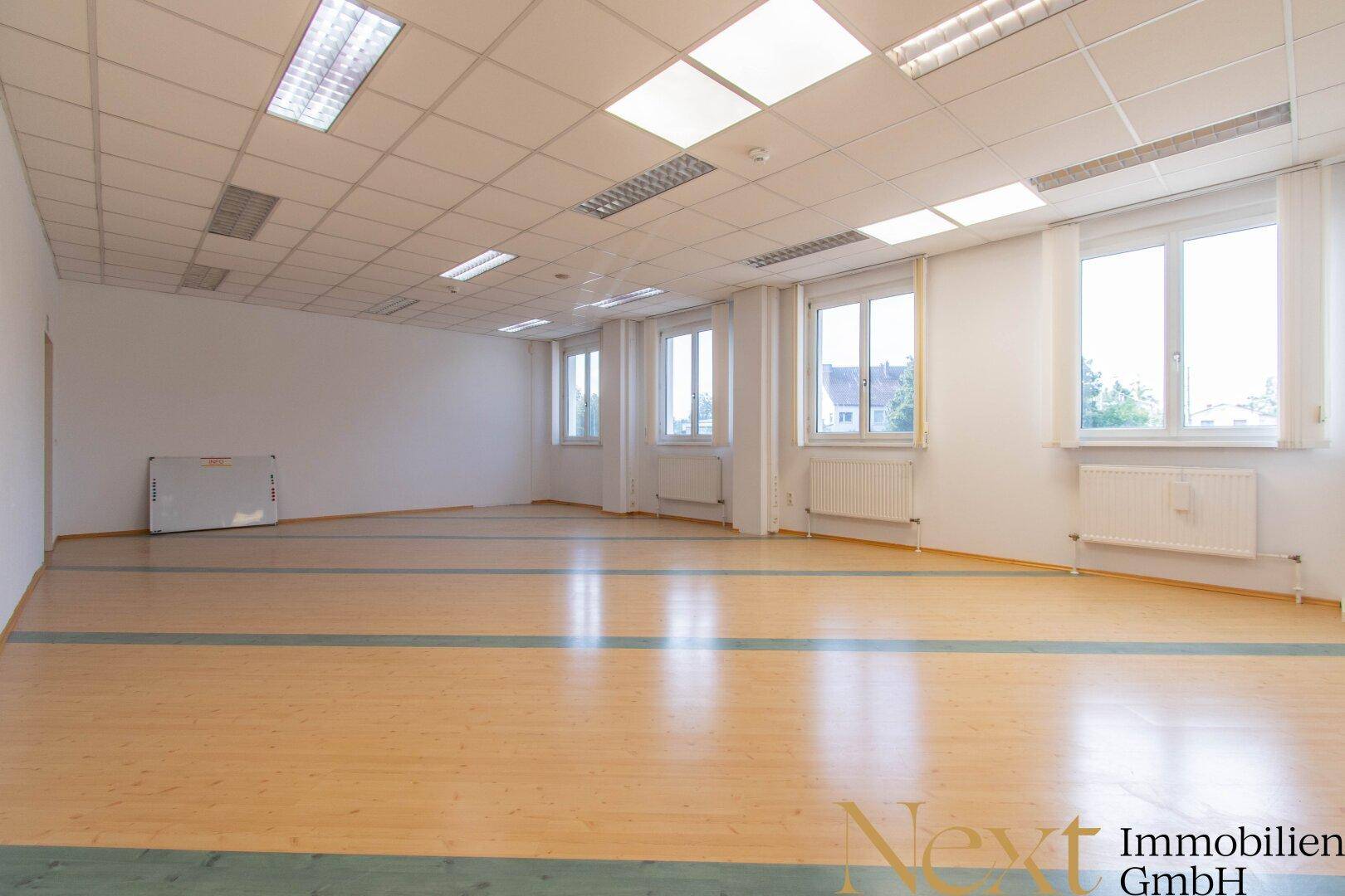 Helles Büro mit Laminatboden und mehreren Fenstern, bietet viel Tageslicht und eine flexible Raumgestaltung.