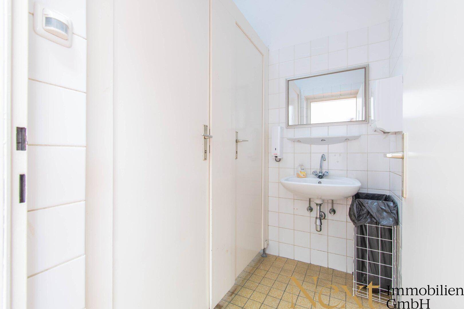 Kleiner Waschraum mit Fliesenboden, Waschbecken und Spiegelschrank, funktional und sauber.