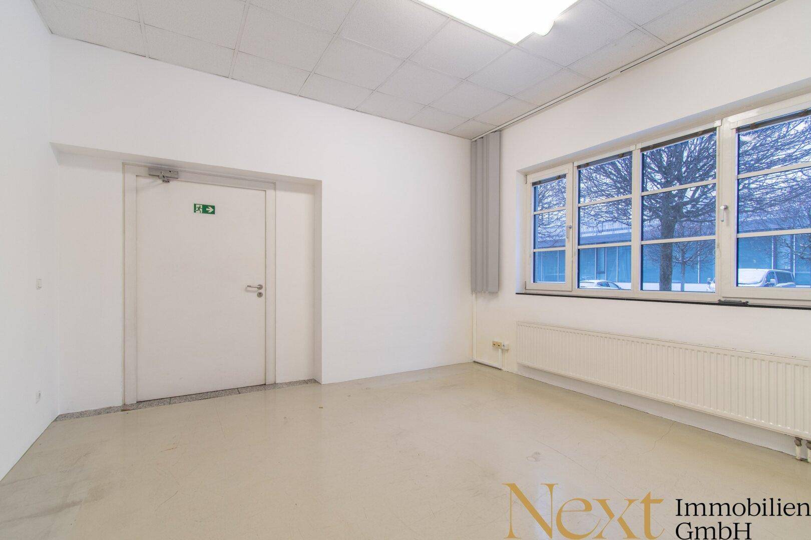 Kleinerer Büroraum mit Fenster, Heizung und einer Sicherheitstür.