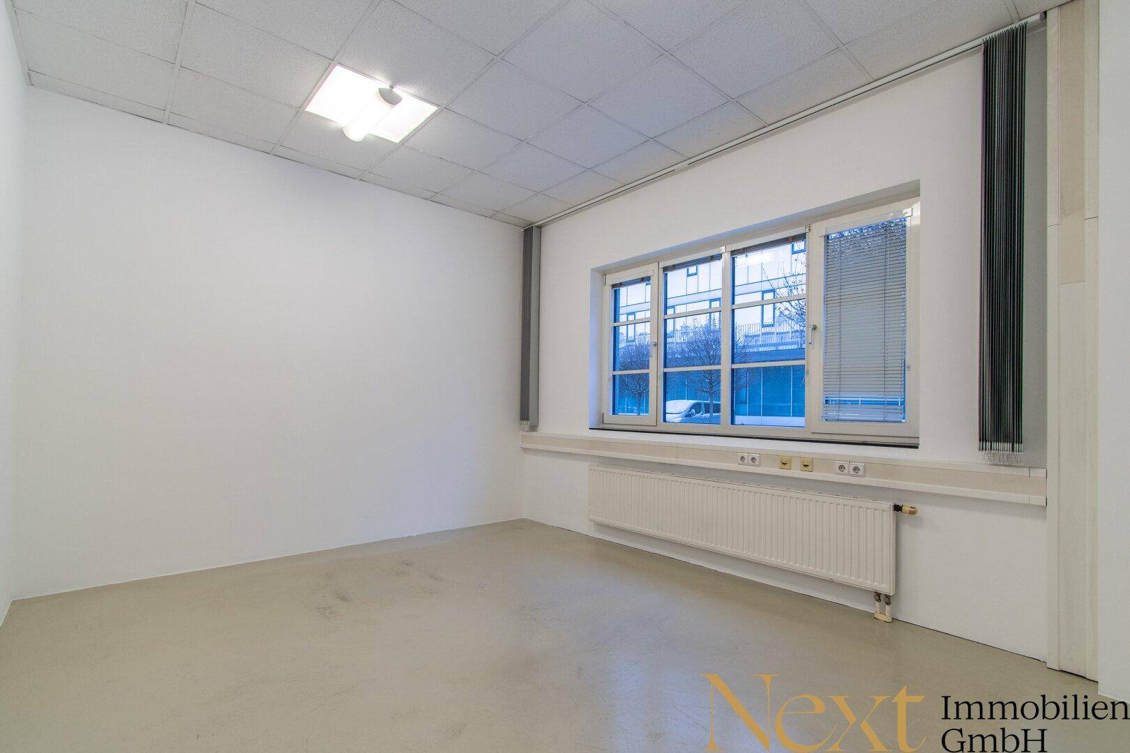 Heller Büroraum mit großem Fenster, Heizkörper und Jalousien für Privatsphäre.