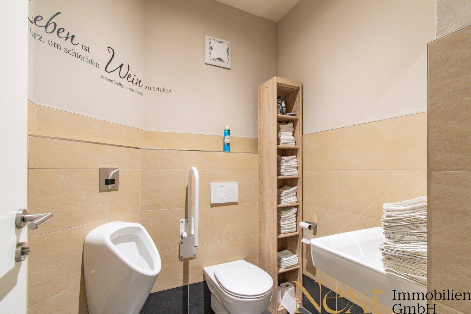 Barrierefreie Toilette mit Urinal, Haltegriffen und beigefarbenen Wandfliesen für Komfort.