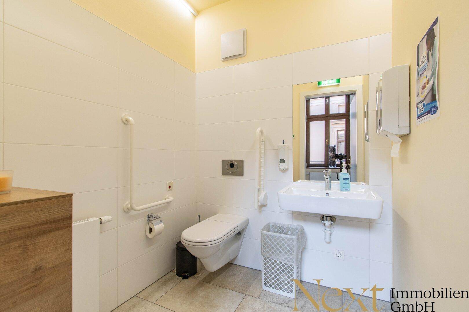 Barrierefreies Badezimmer mit Wand-WC, Waschbecken und Haltegriffen, ausgestattet für Komfort und Zugänglichkeit.