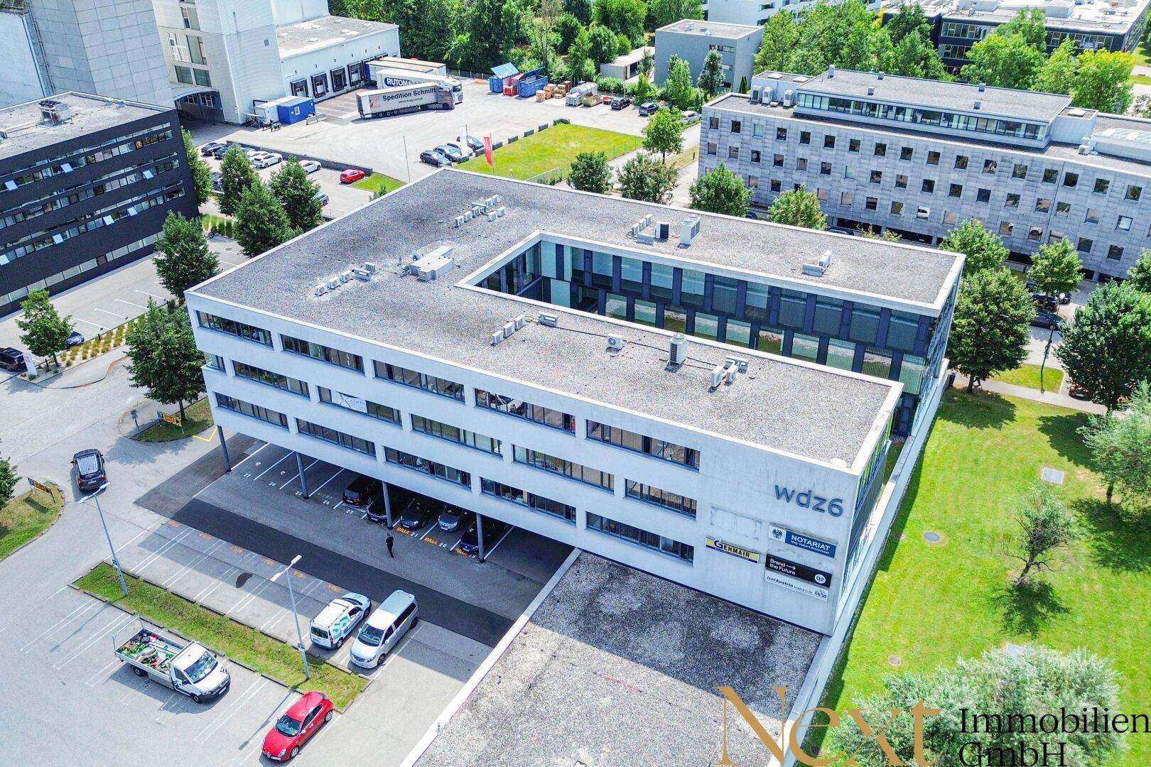 Luftaufnahme des modernen Bürogebäudes mit umliegenden Grünflächen und Parkplätzen in Gewerbegebiet.
