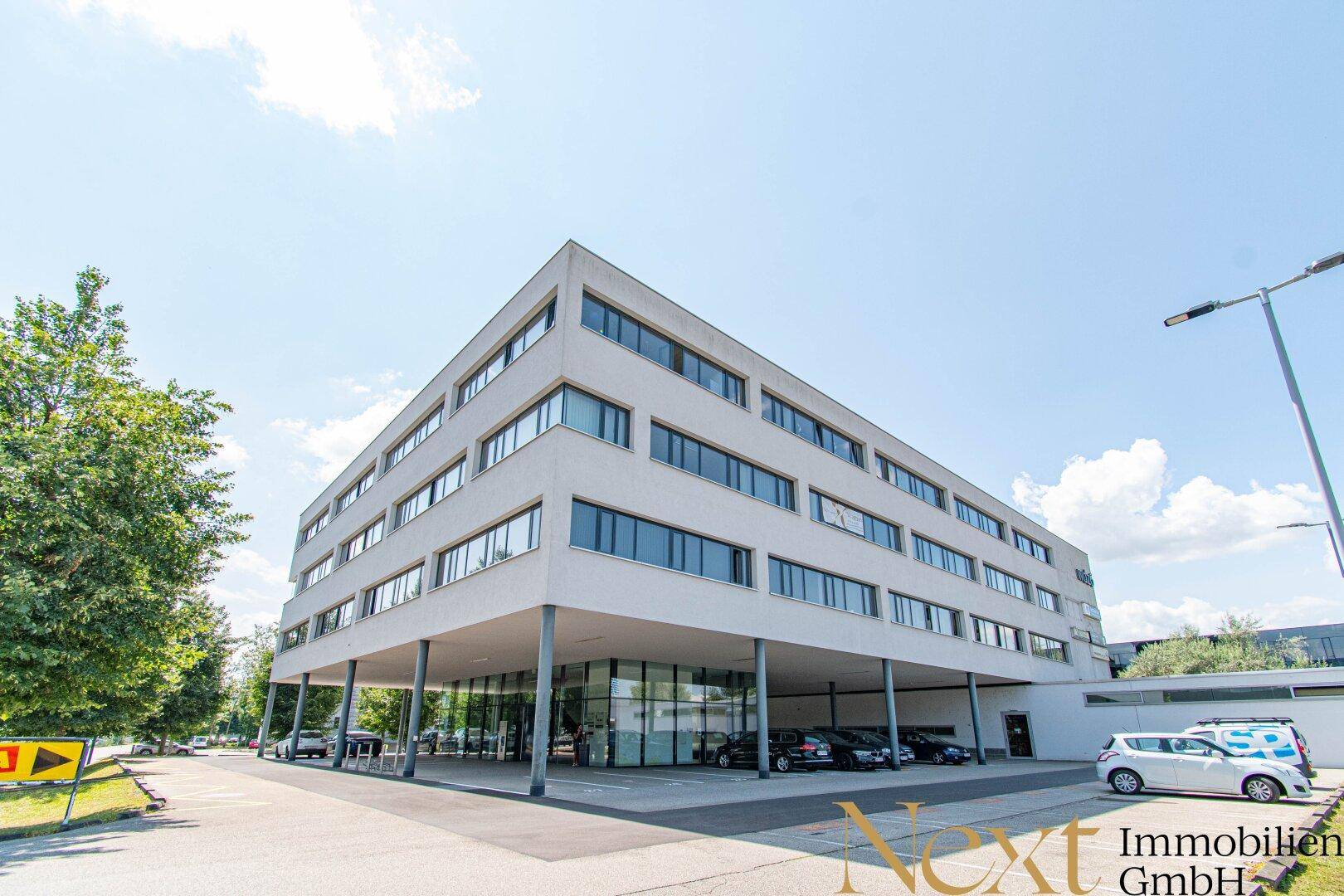 Modernes Bürogebäude mit weißer Fassade und großzügigen Parkmöglichkeiten unter dem Gebäude.