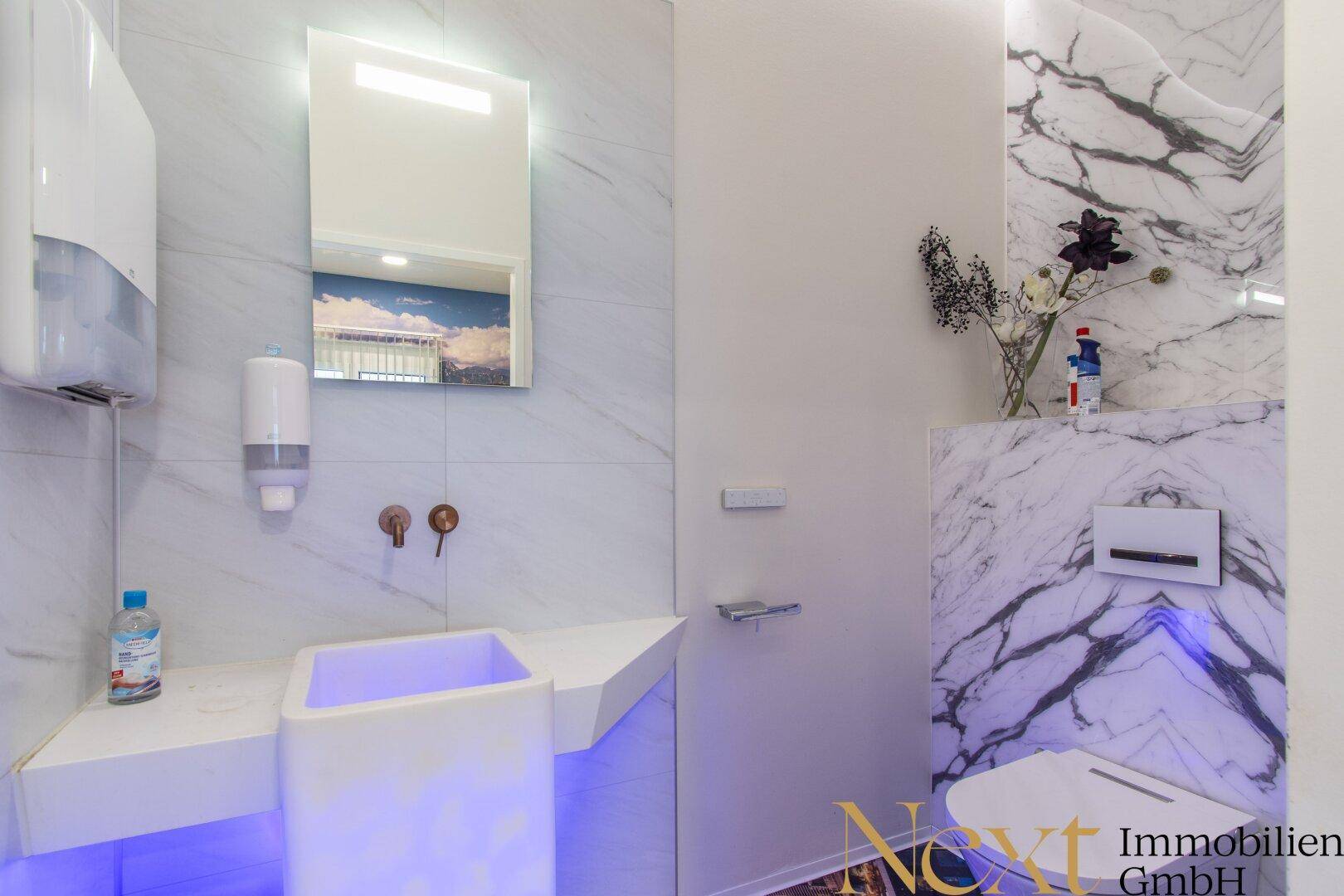 Modernes WC mit Marmorfliesen, stilvollem Waschbecken und indirekter Beleuchtung, das ein luxuriöses Ambiente schafft.
