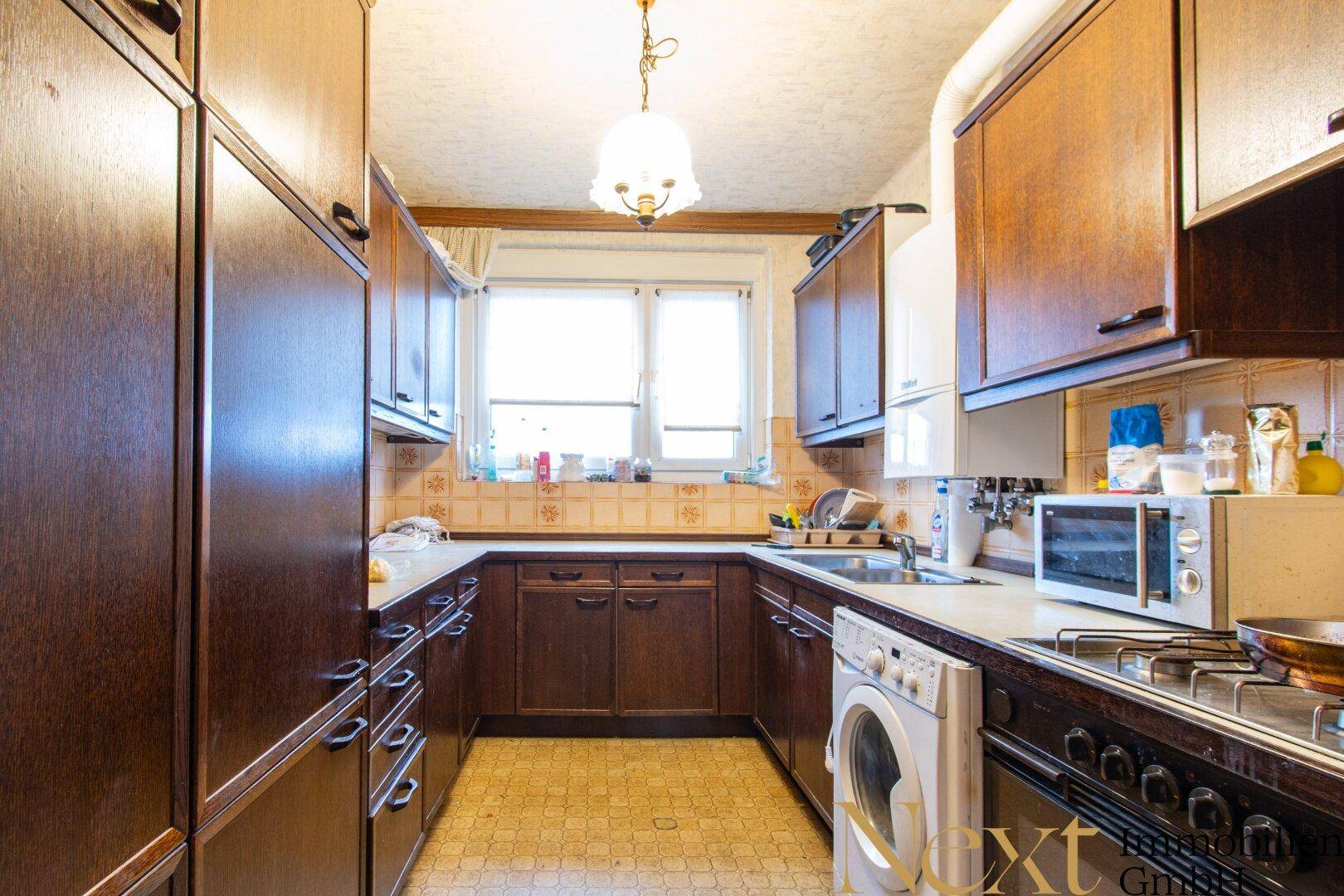 Funktionale Küche mit Holzschränken, Fliesenboden und Fenster.