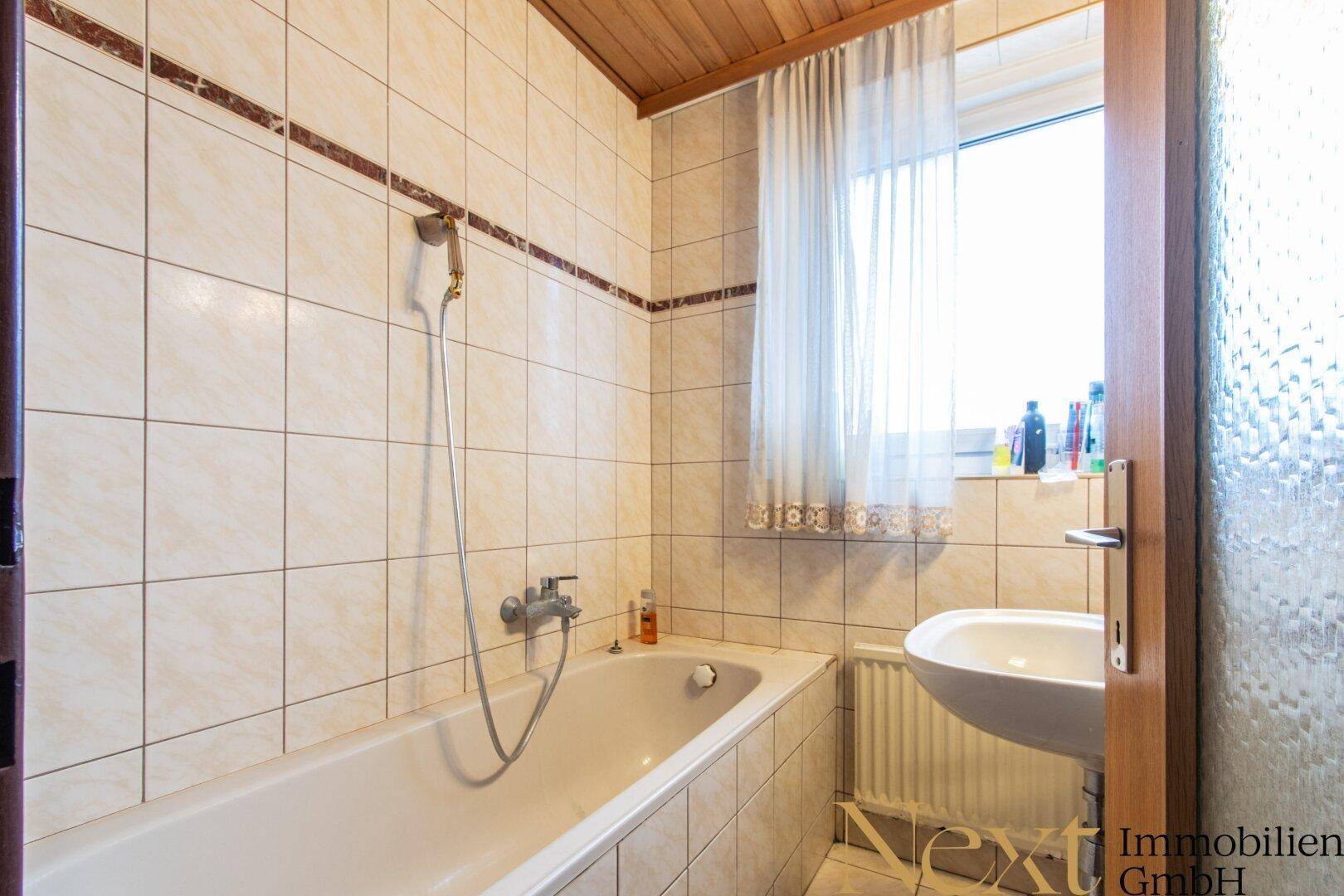 Badezimmer mit Badewanne, Waschbecken, hellen Fliesen und Holzdecke.