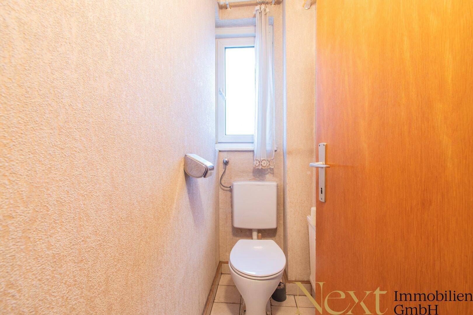 Separate Toilette mit Fenster, hellen Wänden und einfacher Ausstattung.