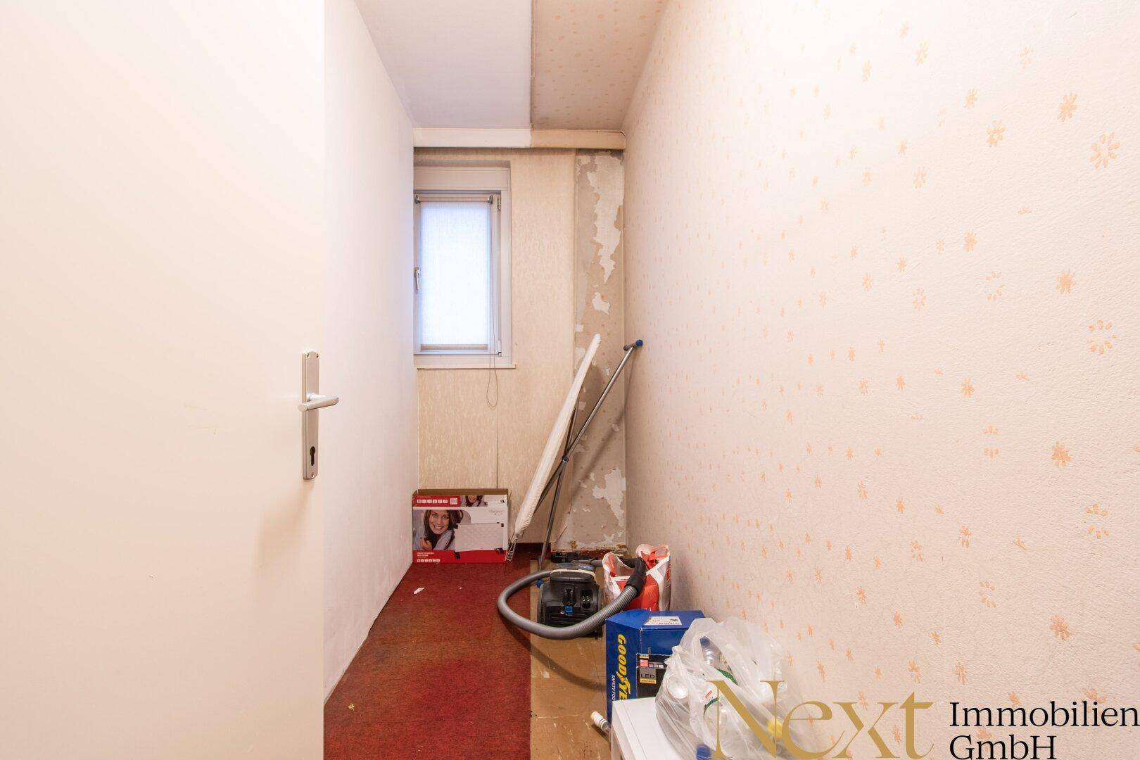 Abstellraum mit Fenster, Tapetenresten und Stauraum für Haushaltsgeräte.