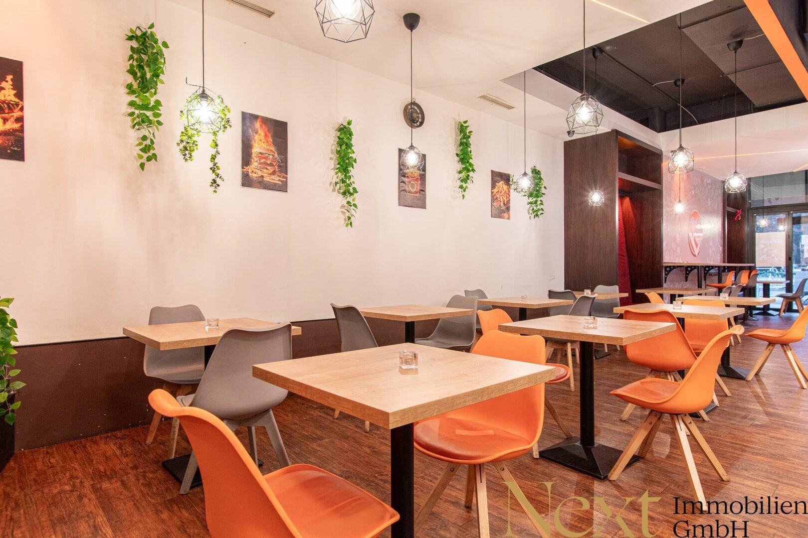Heller Restaurantbereich mit zahlreichen Tischen und Stühlen, dekoriert mit Hängepflanzen und Wandbildern.