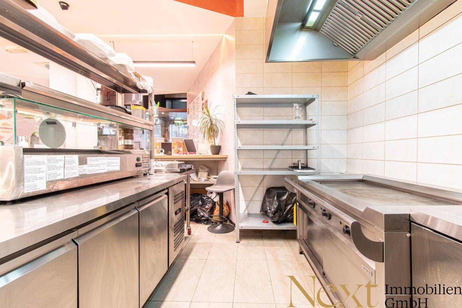 Professionelle Restaurantküche mit Edelstahlgeräten, Abluftsystem und gefliesten Wänden für effizientes Arbeiten.