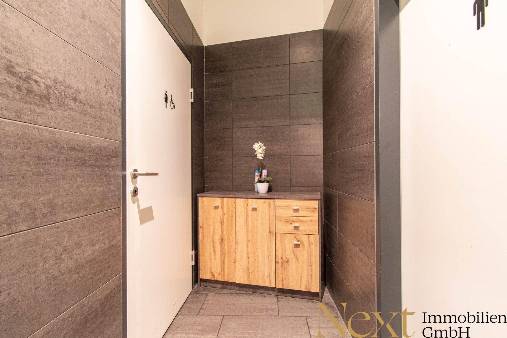 Moderner Toilettenbereich mit dunklen Fliesen, Holzelementen und klaren Hinweisschildern an den Türen.
