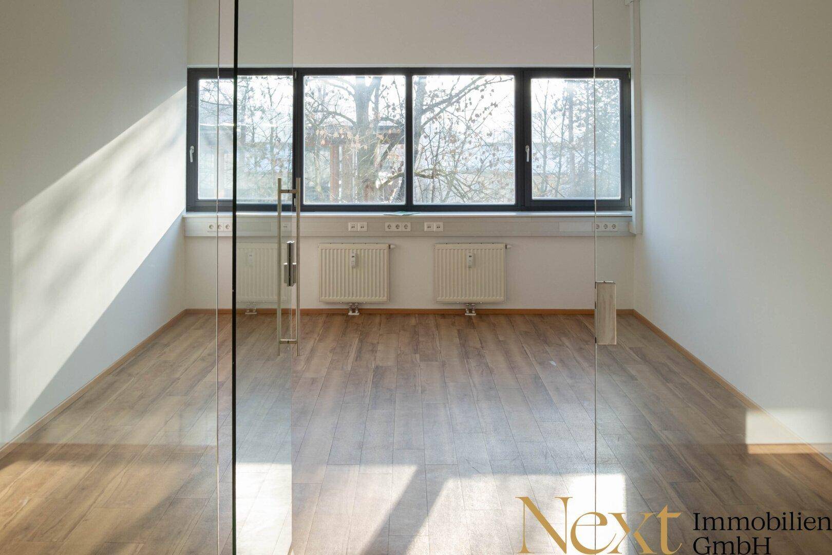 Leeres Büro mit großen Fenstern, Holzboden und Heizkörpern, bereit zur individuellen Gestaltung.
