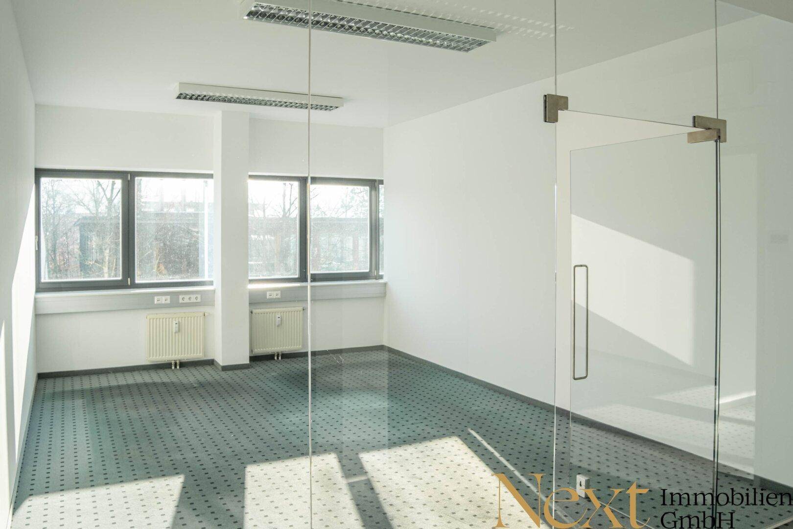 Modernes Büro mit Teppichboden, großen Fenstern und Glaswand, bietet viel Tageslicht.