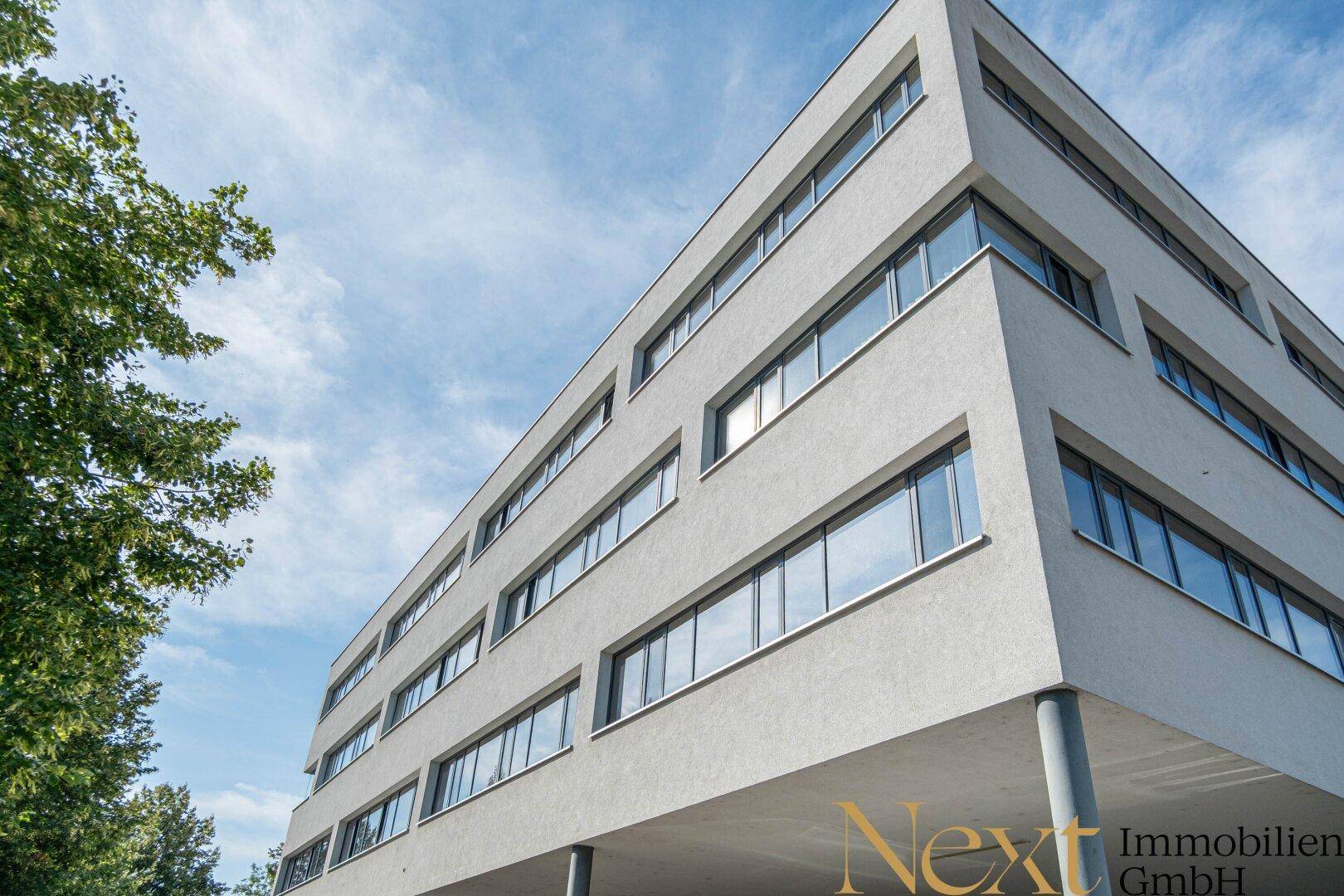 Moderne Bürogebäude-Fassade mit vielen Fenstern und klarem Himmel im Hintergrund.