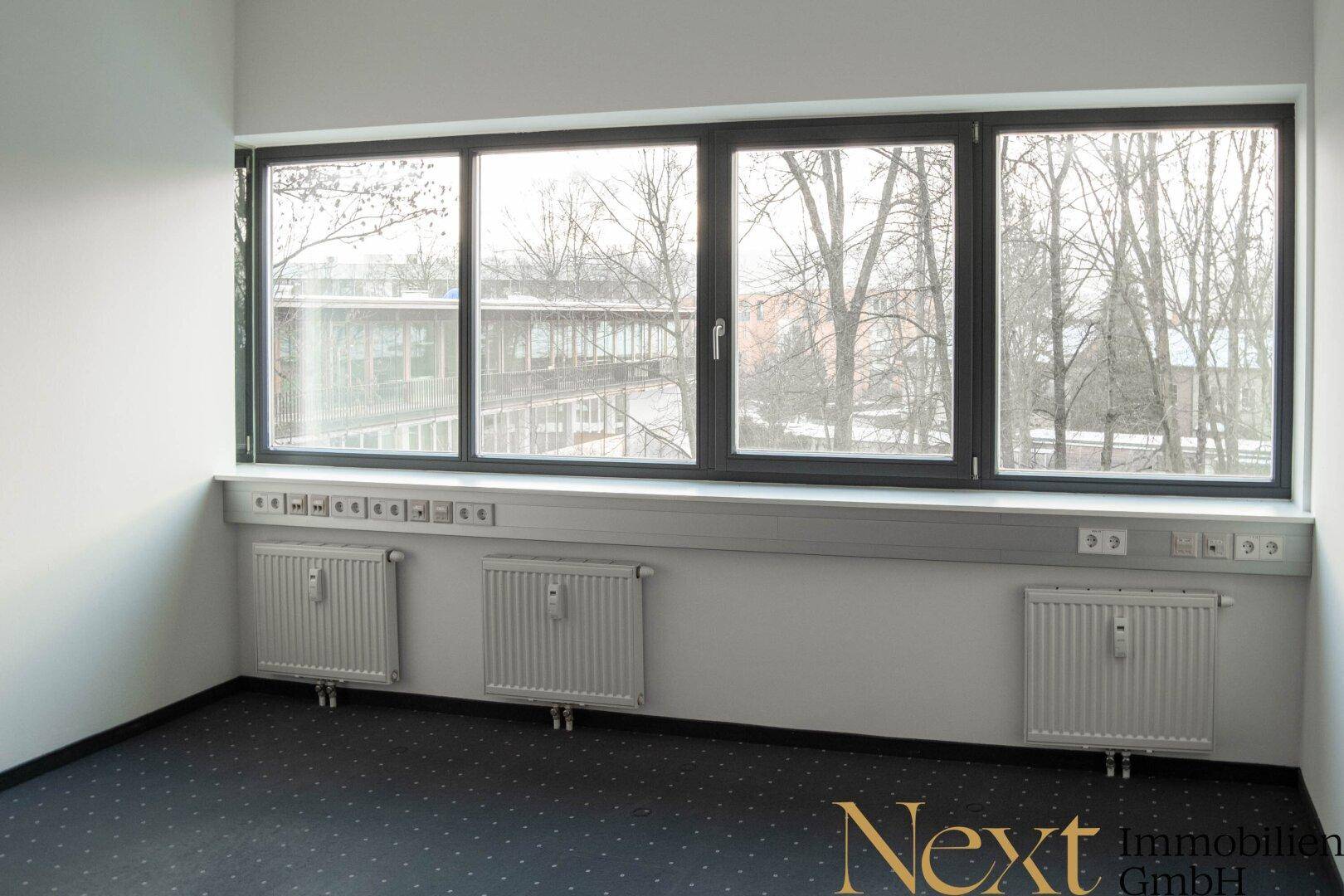 Geräumiges Büro mit großen Fenstern, Heizkörpern und vielen Steckdosen entlang der Wand.