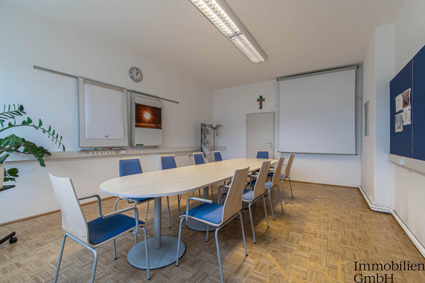 Großer Konferenzraum mit ovalem Tisch, vielen Stühlen und Whiteboards für Besprechungen.