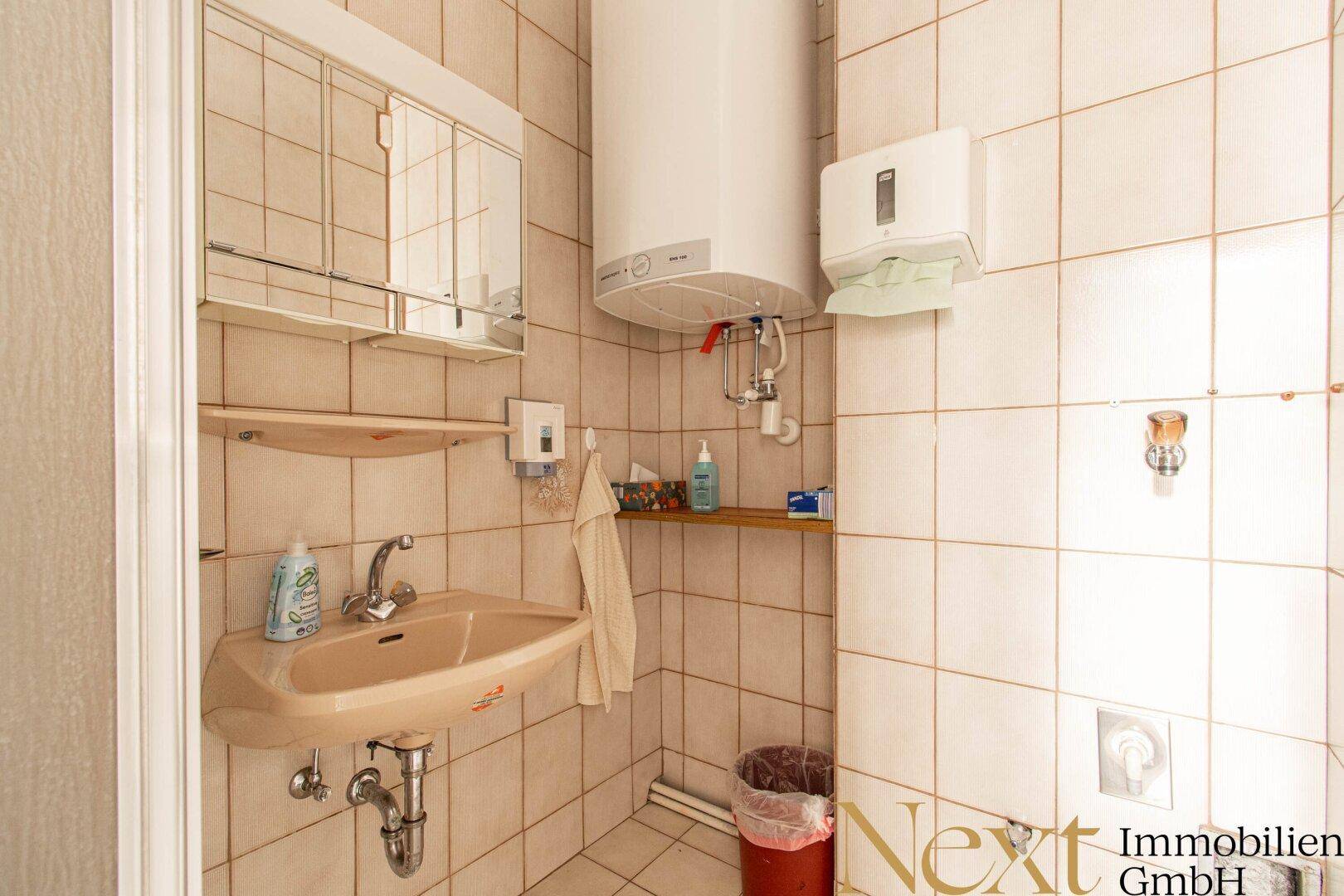 Badezimmer mit Waschbecken, Spiegelschrank und Warmwasserboiler, gefliesten Wänden und Boden.