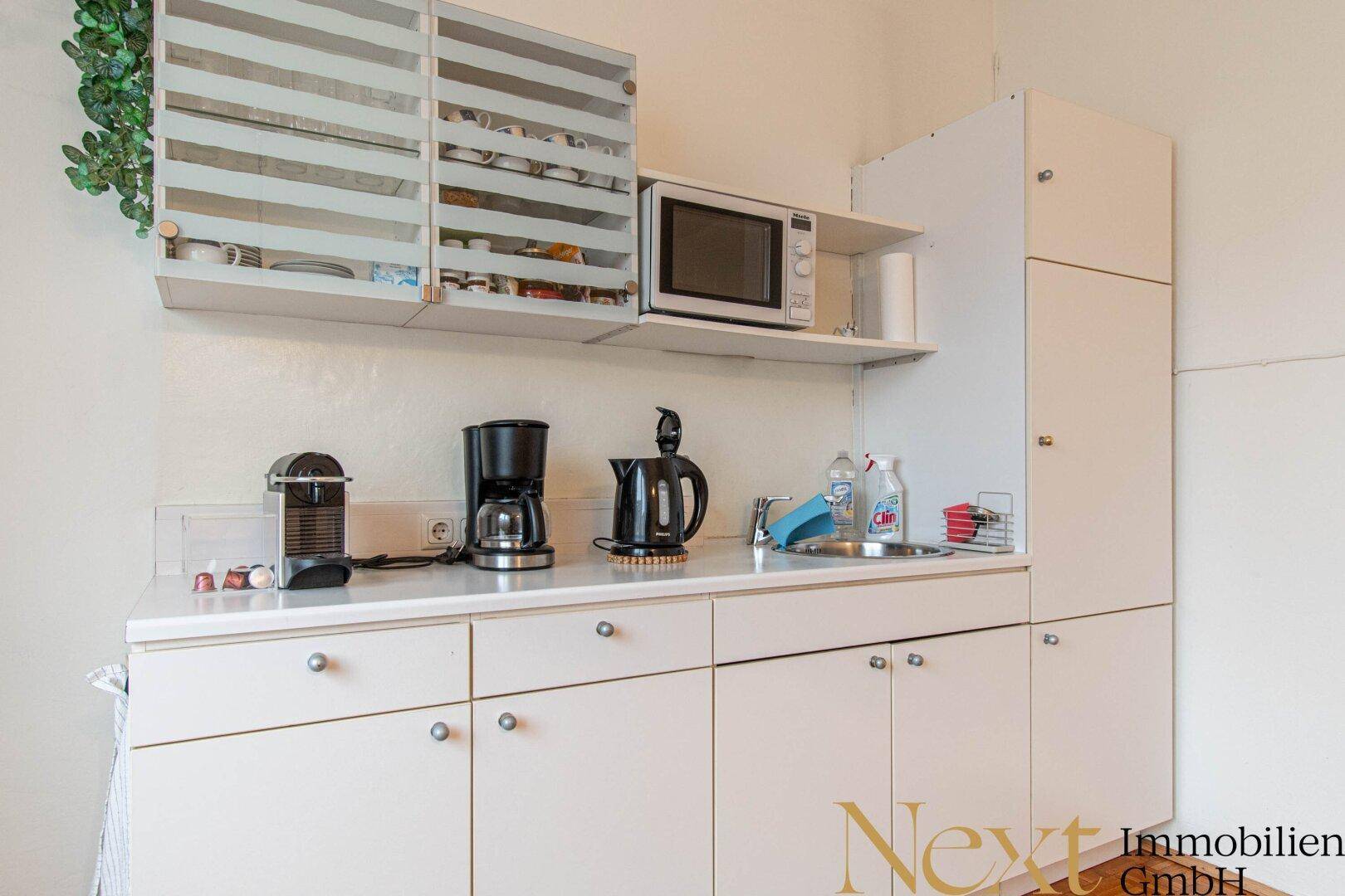 Detailansicht der Küchenzeile mit weißen Schränken, Mikrowelle und Kaffeemaschinen.