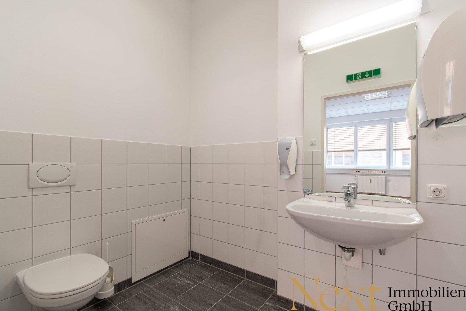 Funktionale Toilette mit weißen Fliesen an den Wänden und einem Waschbecken, ausgestattet für den täglichen Gebrauch.