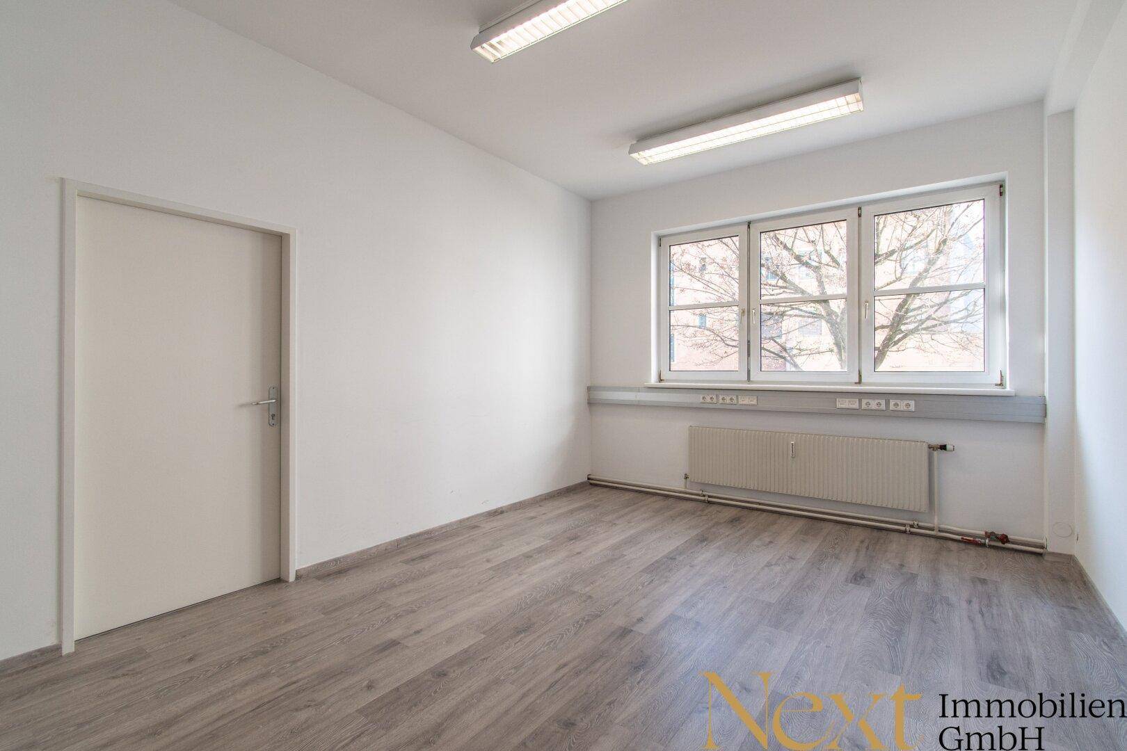 Geräumiges Büro mit hellem Laminatboden, weißen Wänden und einer modernen Tür.