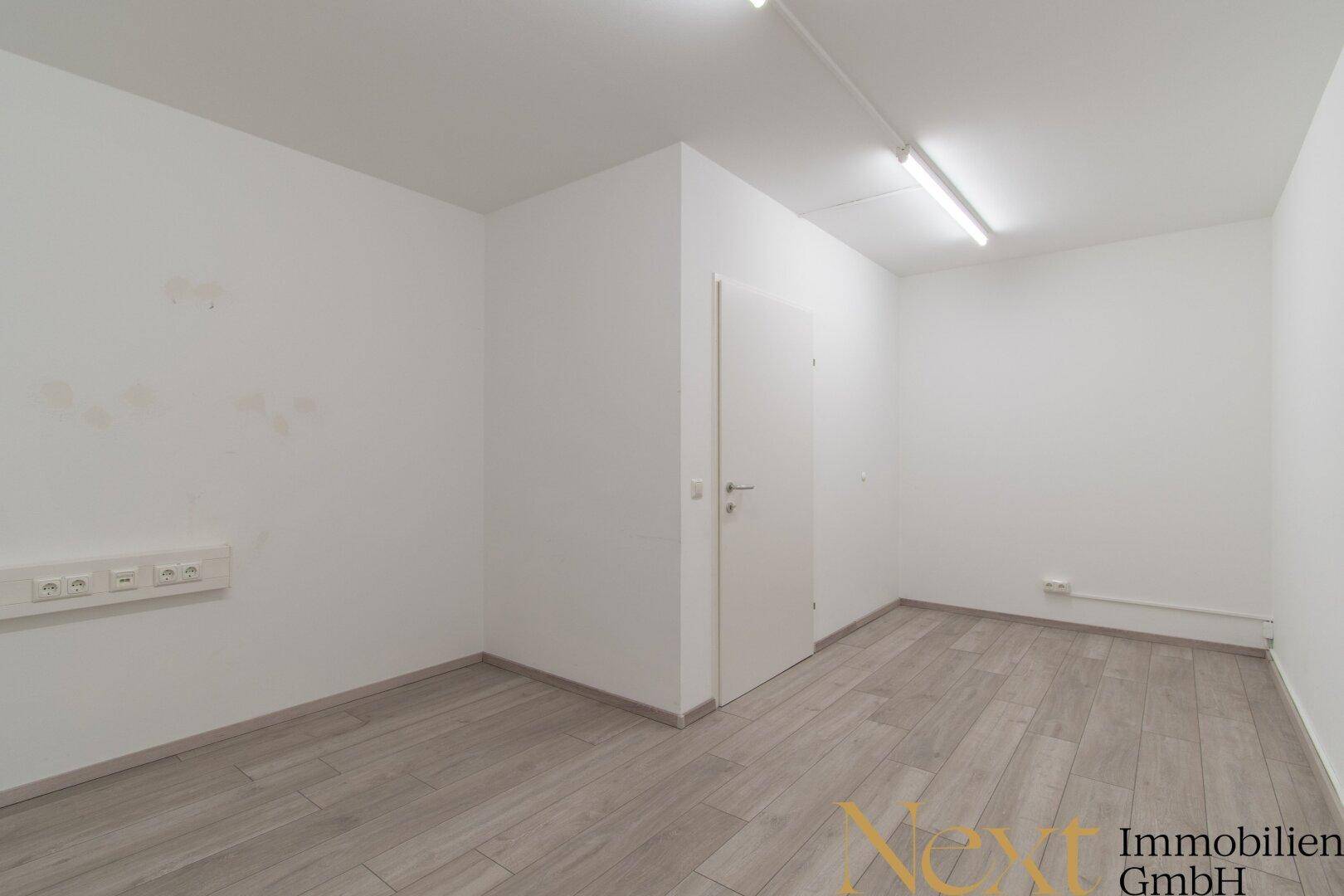 Funktionaler Raum mit weiß gestrichenen Wänden, hellem Boden und einer einfachen Tür, geeignet als kleines Büro oder Abstellraum.